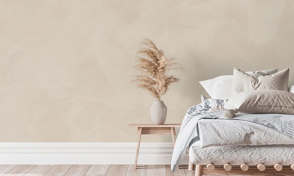 Chenil avec un lit fait de draps blancs, plusieurs oreillers, et un coussin. À côté, une petite table en bois avec un vase contenant des herbes séchées.