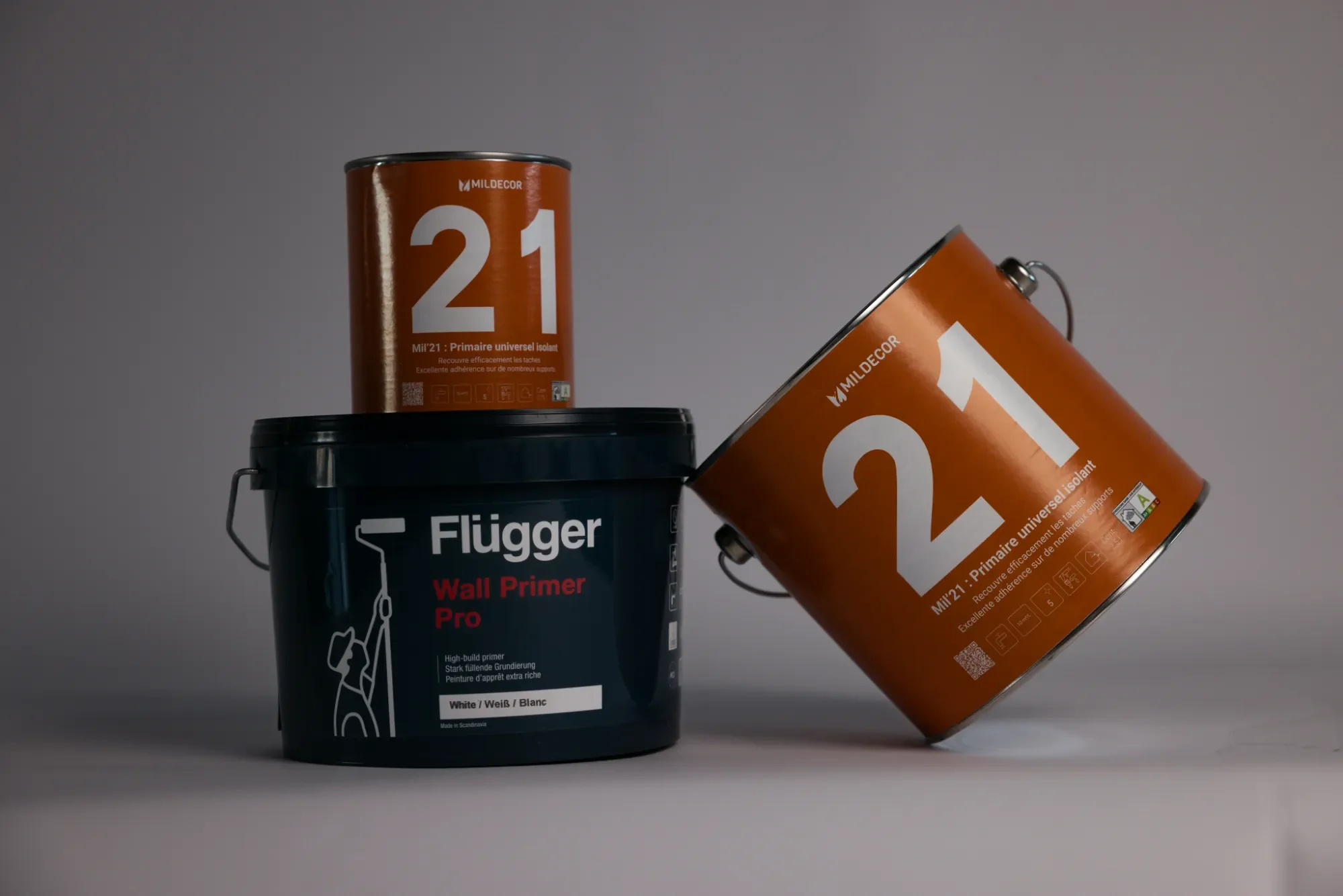 Trois pots de peinture, dont deux orange avec le numéro 21 et un noir avec un rouleau peintre sur l'étiquette, sur un fond gris.