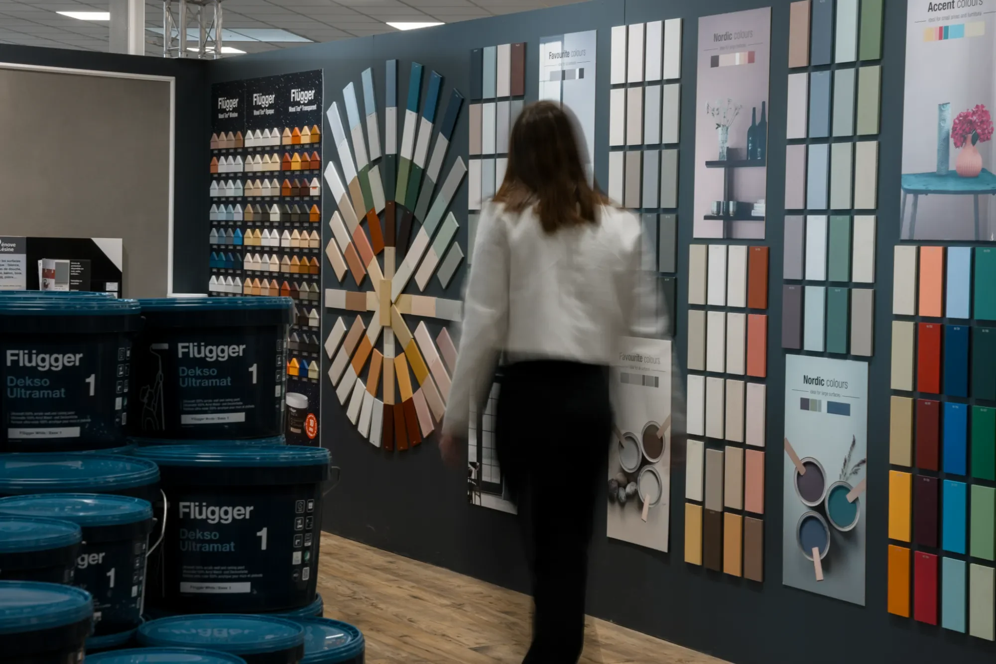 Une femme dans un magasin de peinture observe des panneaux de couleurs et des nuanciers sur un mur.