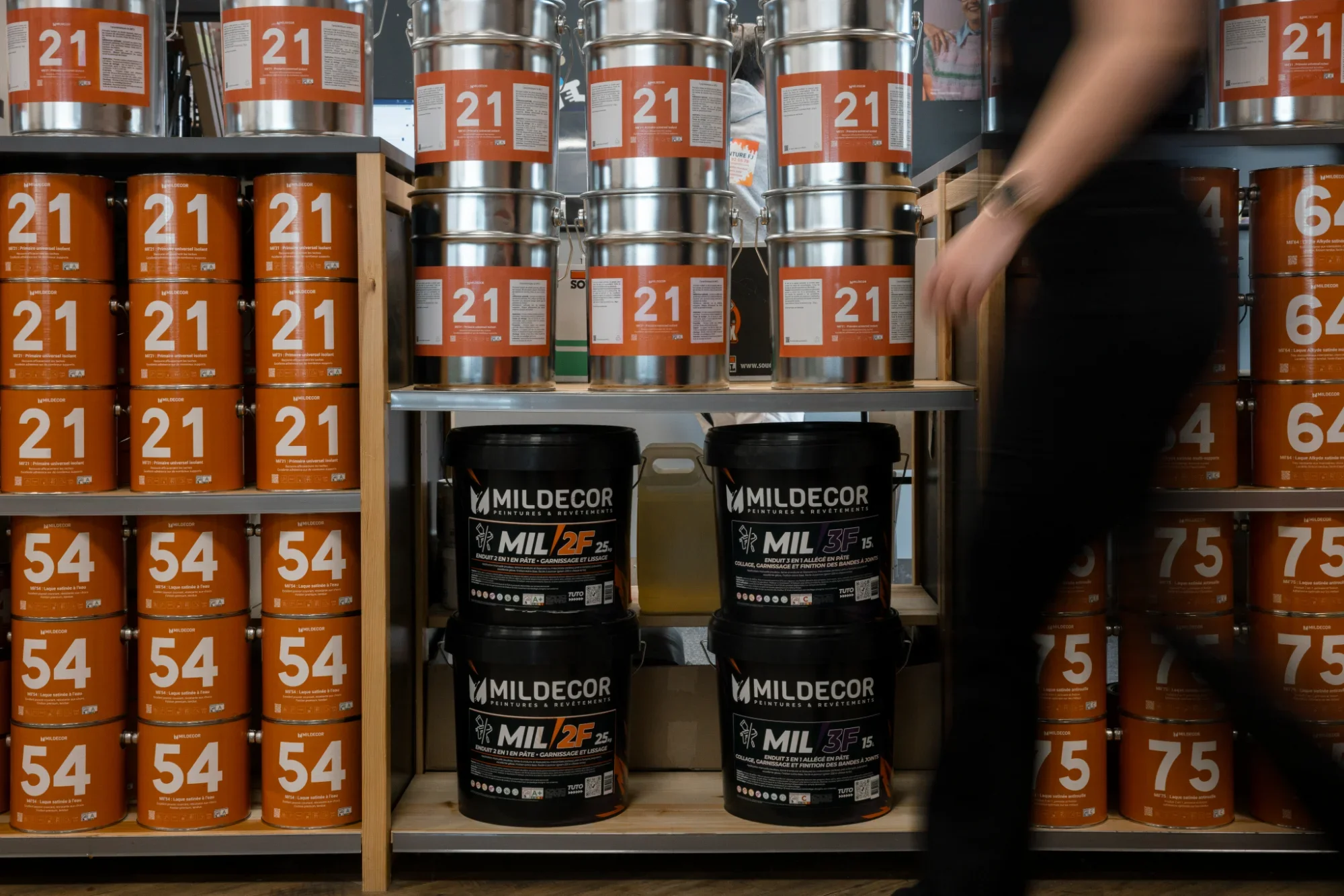 Rayon avec des pots de peinture orange et des seaux de peinture noir, dans un magasin de bricolage.