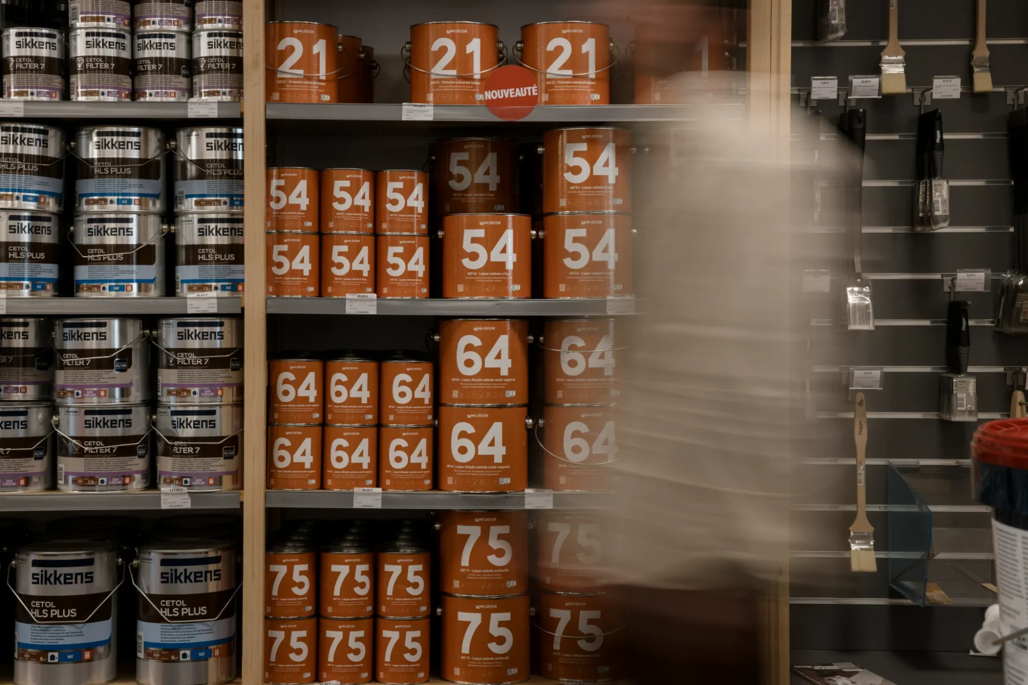 Rayonnage de pots de peinture de différentes couleurs et tailles, notamment en orange et en blanc, dans un magasin de bricolage.