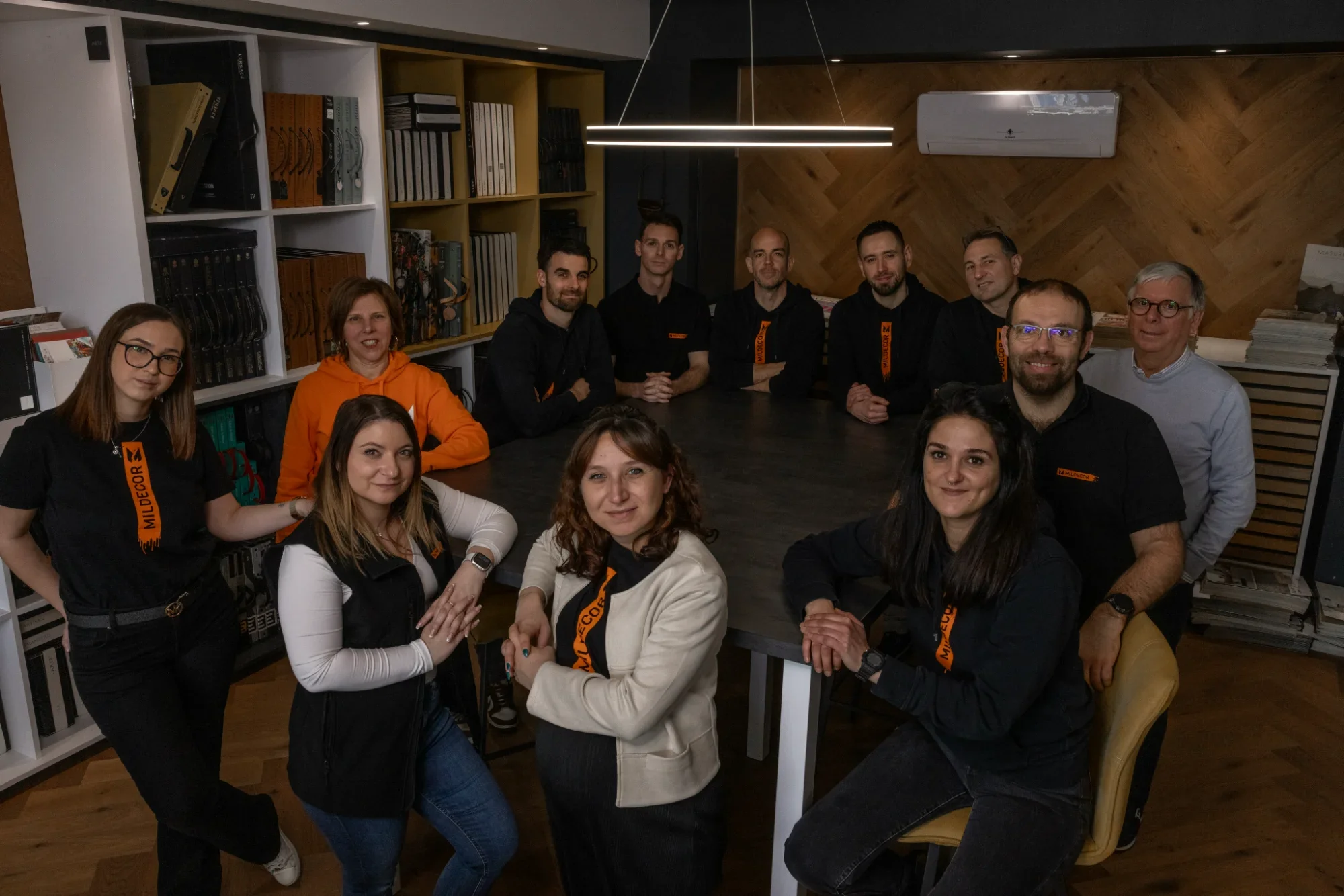 Groupe de personnes en réunion autour d'une grande table dans un bureau, certains portant des vêtements avec le logo Mildecor.