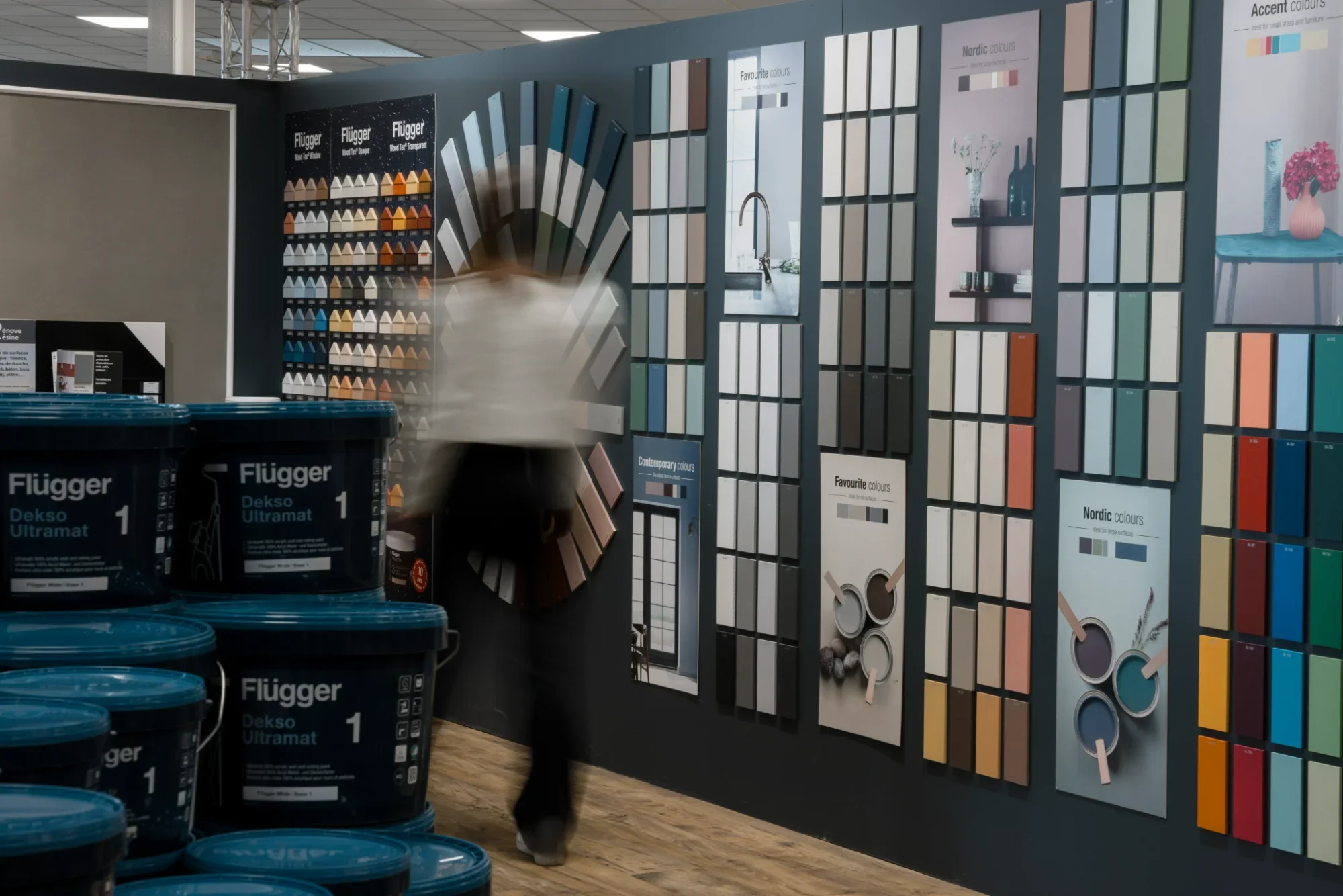 Un magasin de peinture avec des échantillons de couleurs sur un mur et des pots de peinture bleus empilés à gauche.