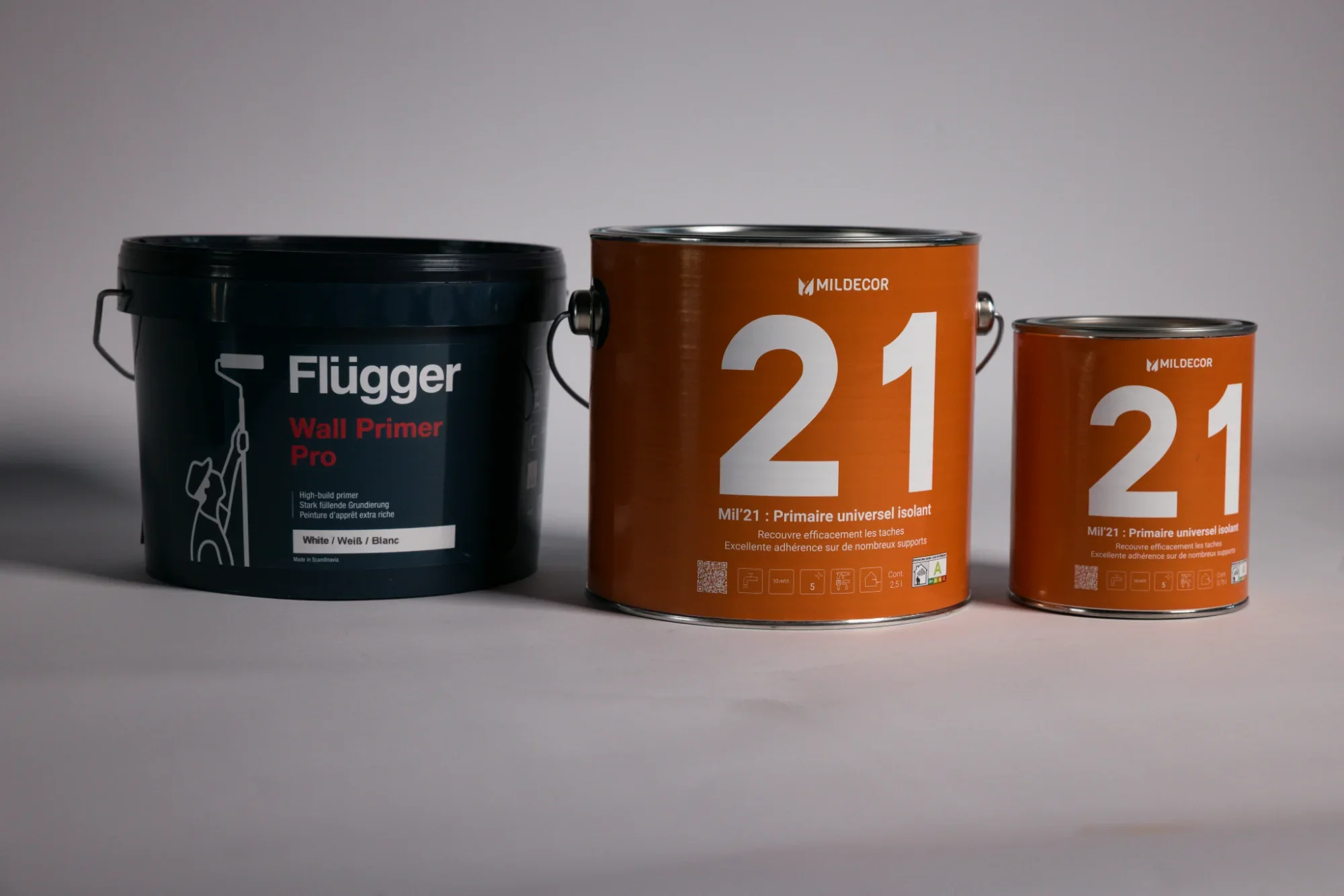 Trois pots de peinture alignés sur une surface blanche, de gauche à droite : un seau noir de Primer Wall Pro, deux pots orange conformes à la marque Mildecor, avec le numéro 21, une grande et une plus petite.