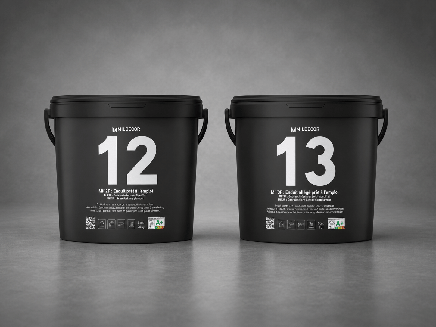Deux boîtes de peinture noires de la marque Mildecor, numérotées 12 et 13, placées côte à côte sur une surface grise. Chaque boîte affiche des informations en français sur le type de peinture et ses caractéristiques.