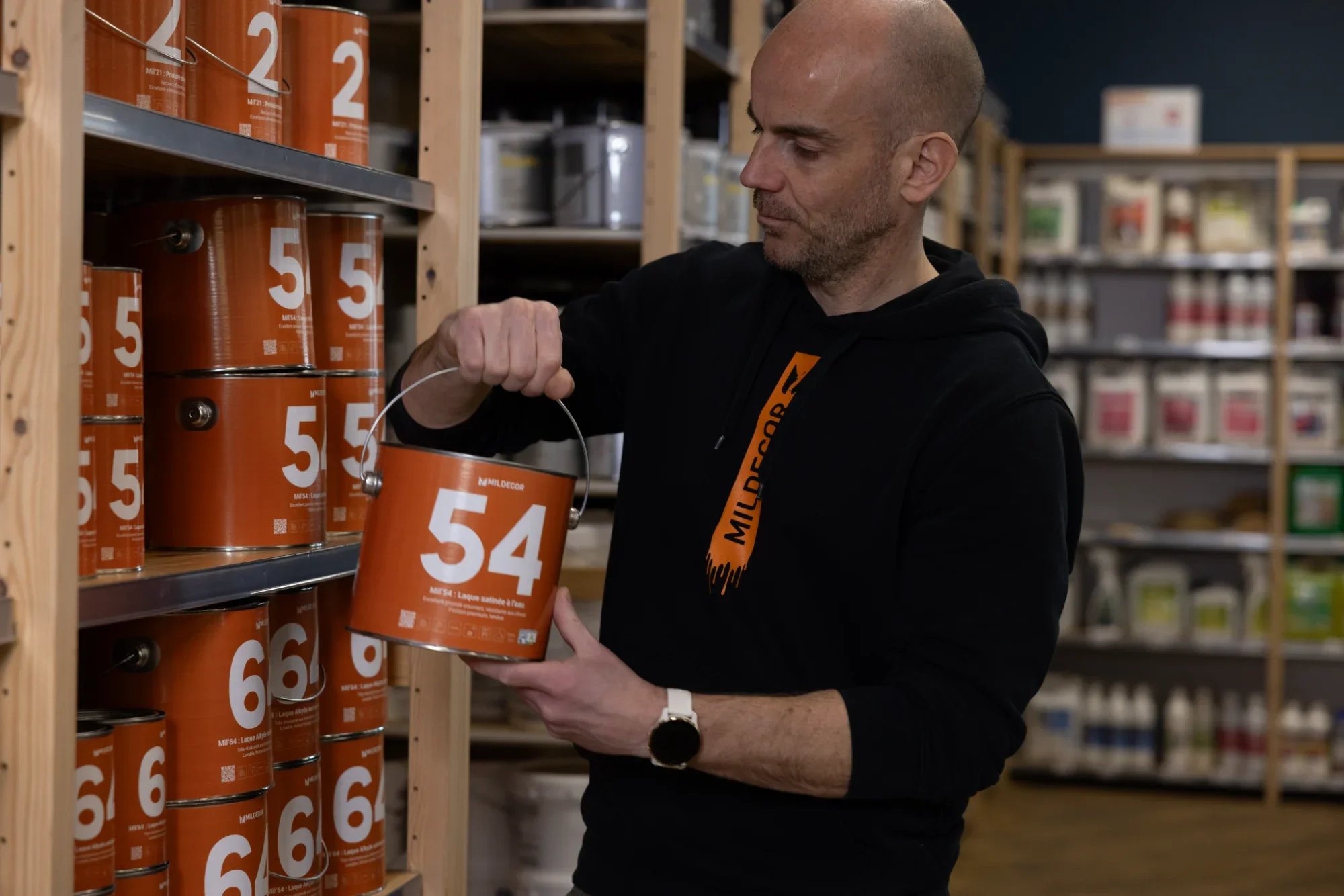 Un homme regarde des pots de peinture orange avec des numéros, dans un magasin de bricolage.