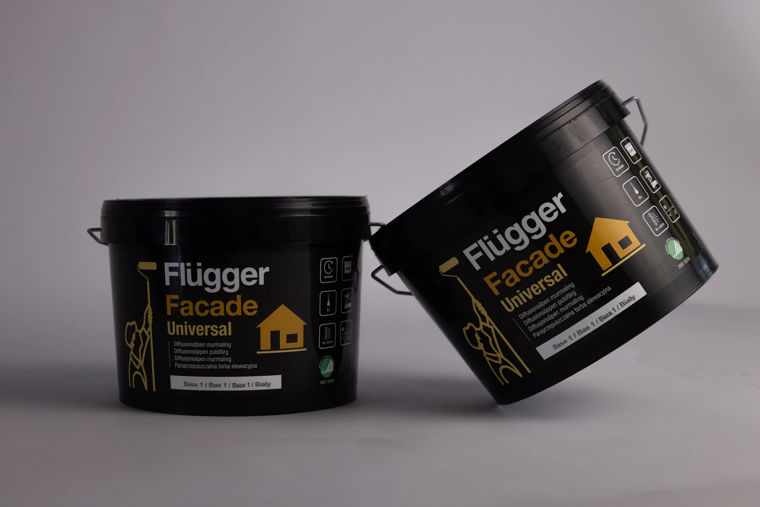 Deux pots de peinture noire de marque Flügger Facade Universel avec étiquettes en français et en polonais, placés contre un fond gris.