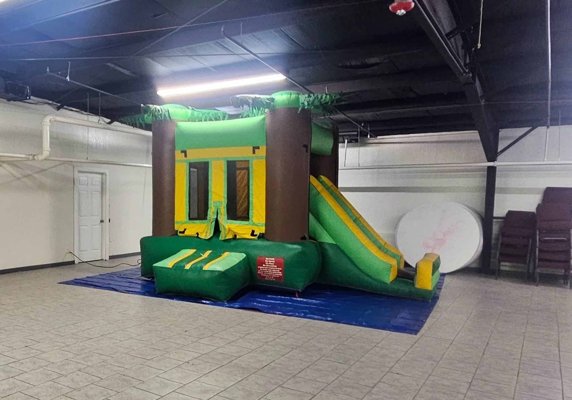 Indoor inflatable jungle gym with green and yellow slides, jungle-themed design, and padded entrance, set on a blue mat.