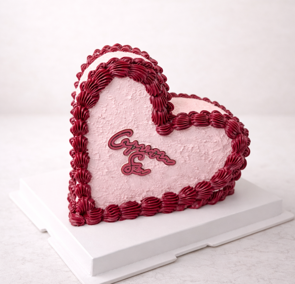 Heart-shaped cake decorated with pink frosting and red piped borders, with an inscription in the center that says 'Congratulations'.