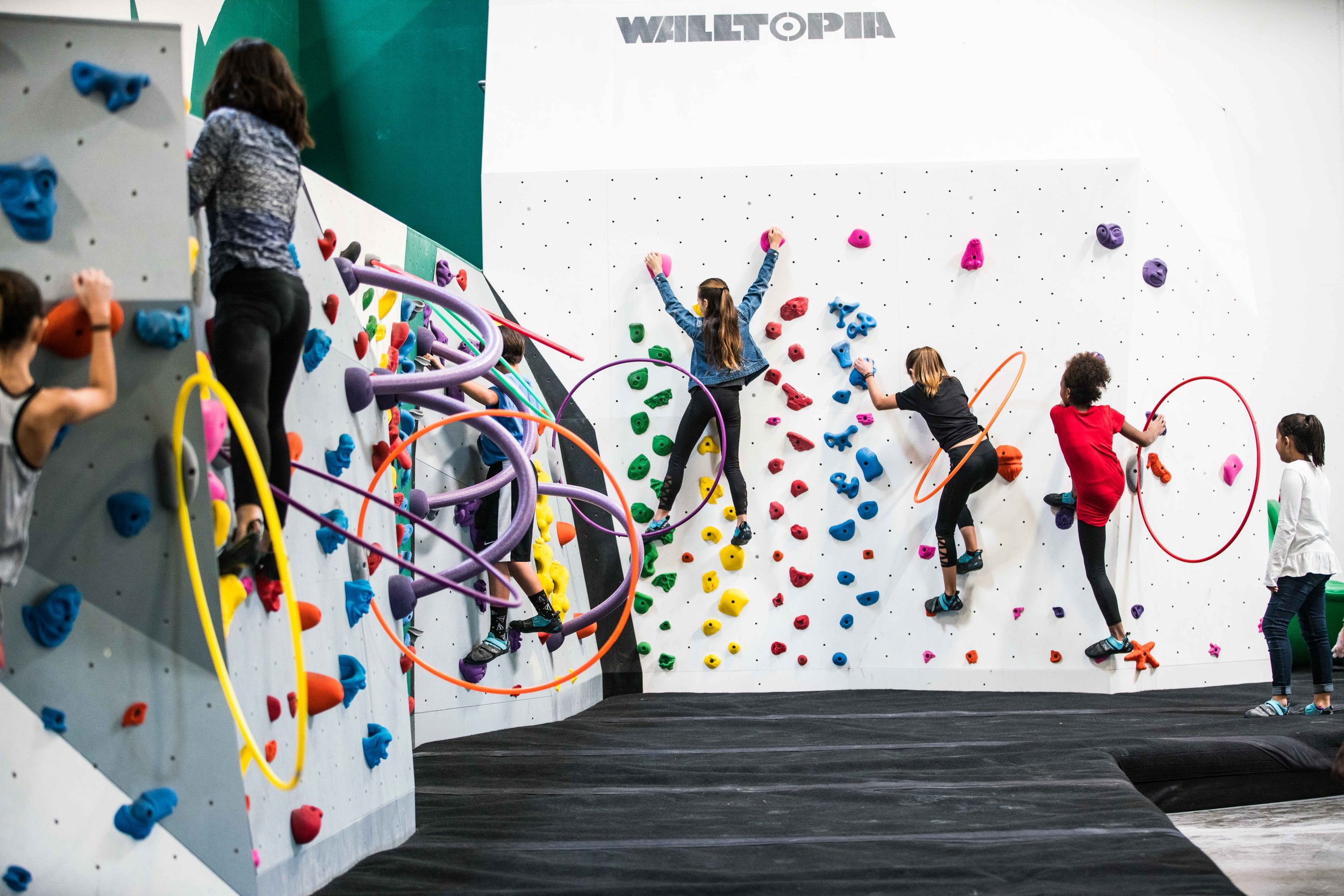 Children climbing a colorful indoor bouldering rock wall.