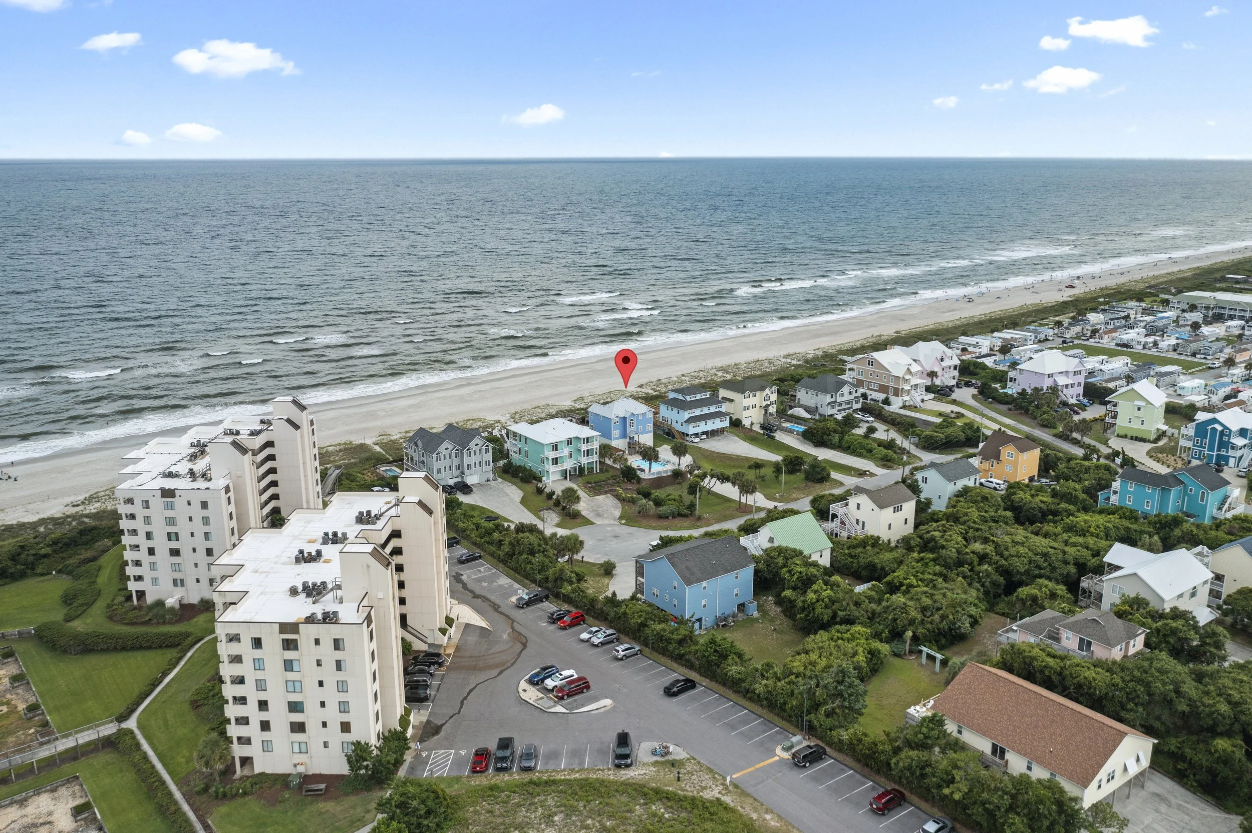 Aerial view of a coastal town with colorful houses, tall apartment buildings, a beach, and the ocean with scattered clouds in the sky.
