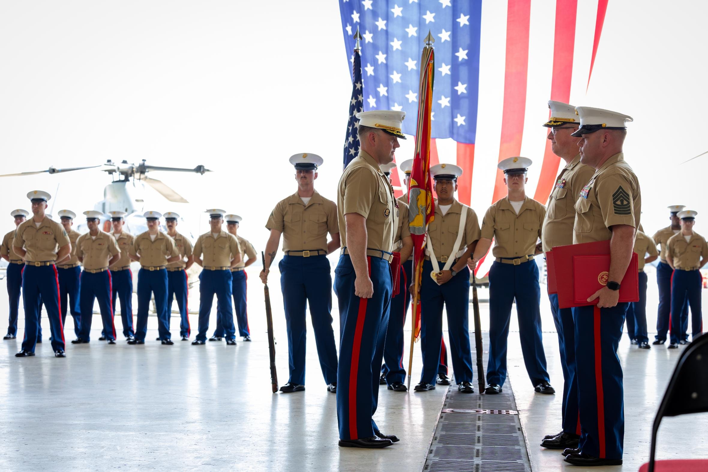 Military personnel standing in formation during a ceremony, with American flags in the background.