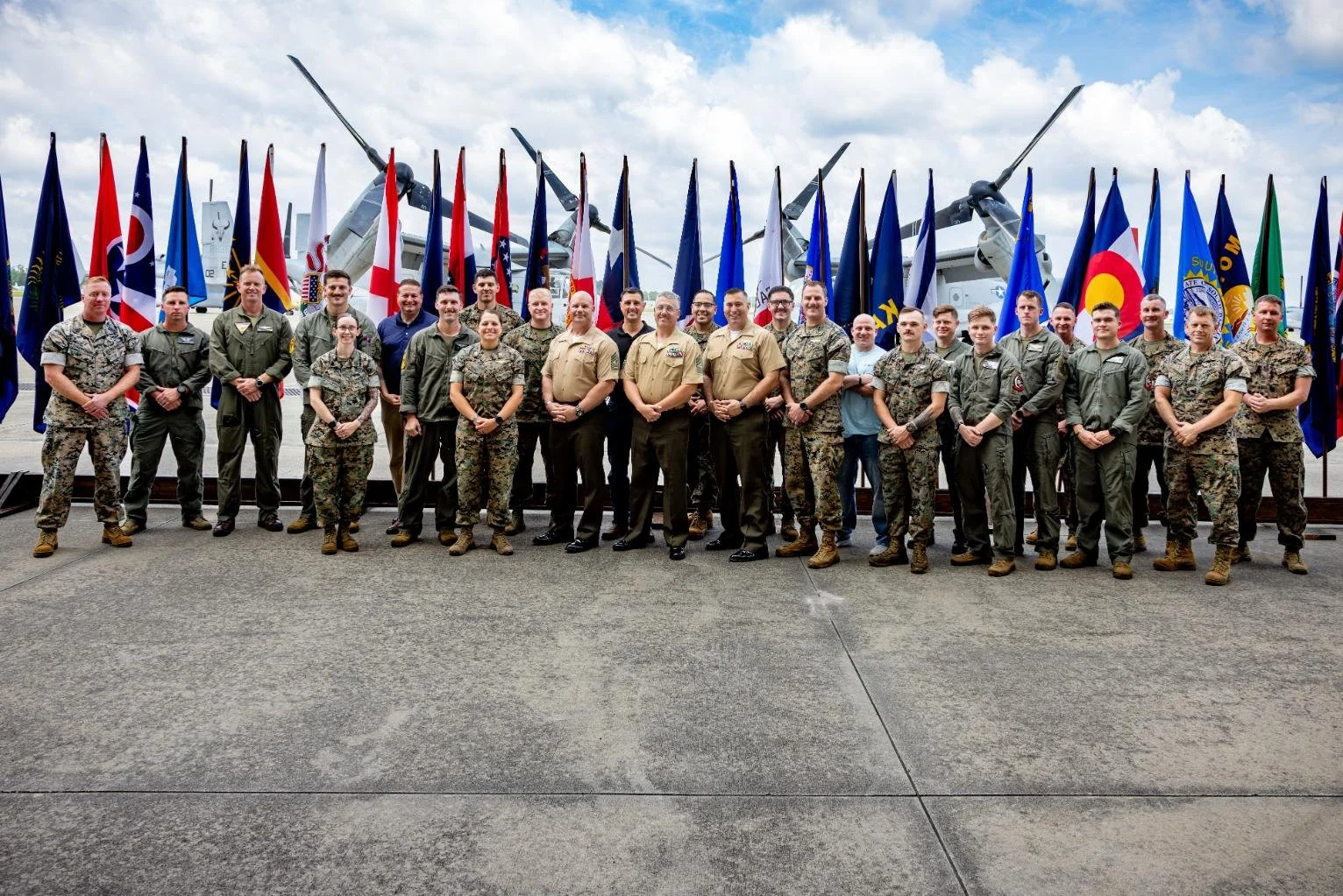 Group of military personnel standing in front of flags and military aircraft.
