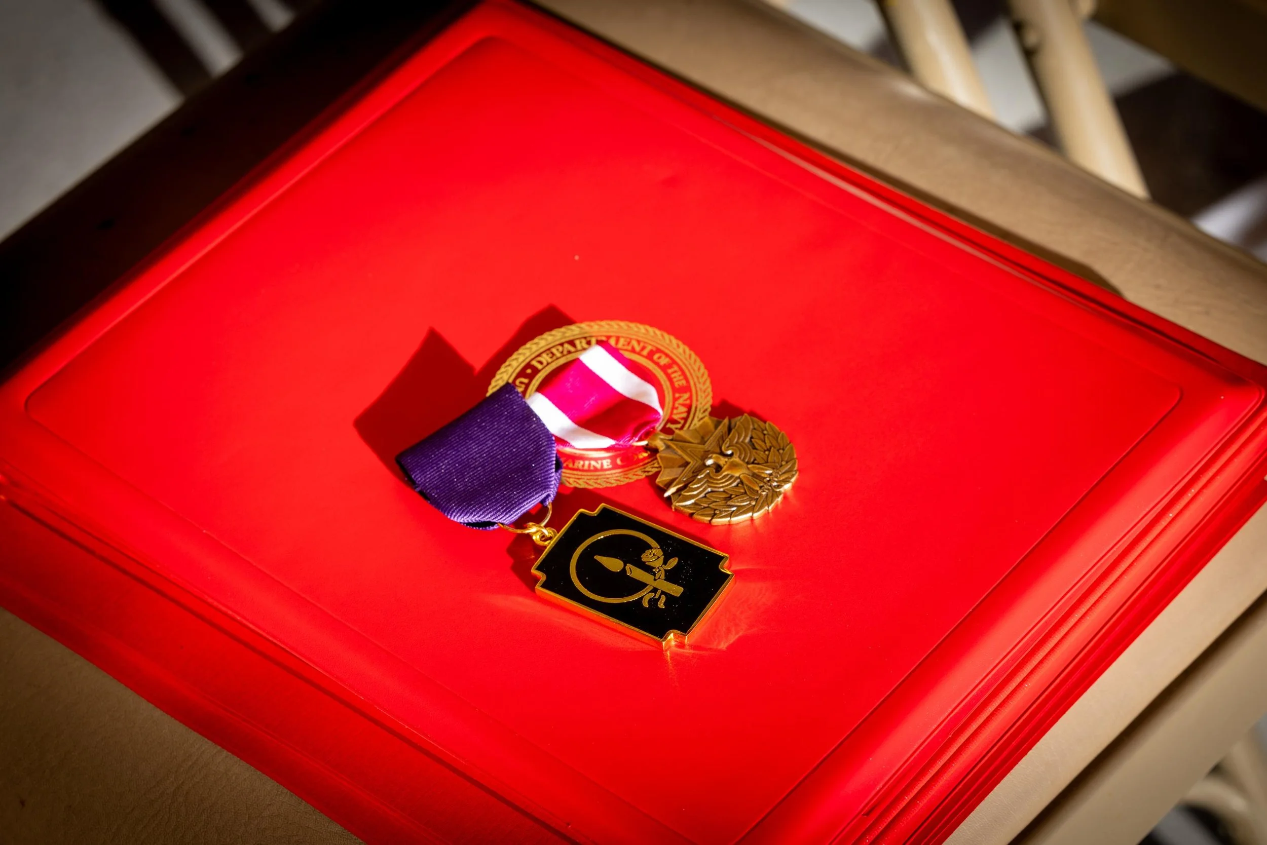 Medal with a star-shaped design, a ribbon in red, white, and purple, placed on a red box.