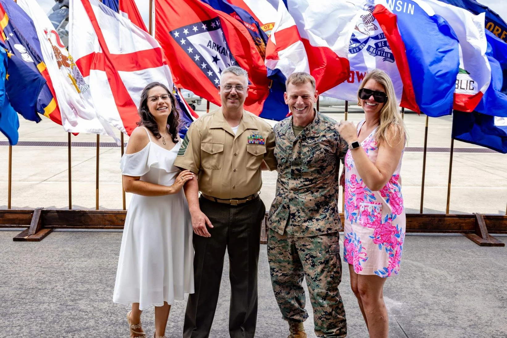 Group of four people standing in front of a display of various national flags at an airport or military base