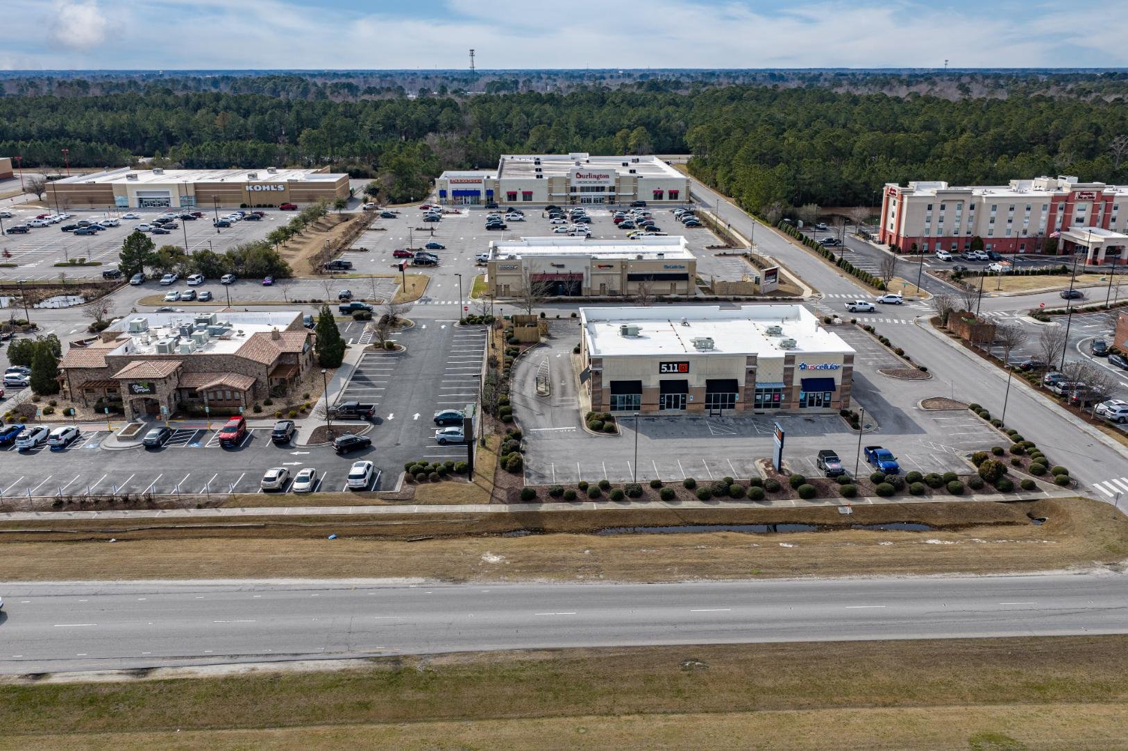 Aerial view of a shopping plaza with multiple stores, parking lots, and surrounding greenery.