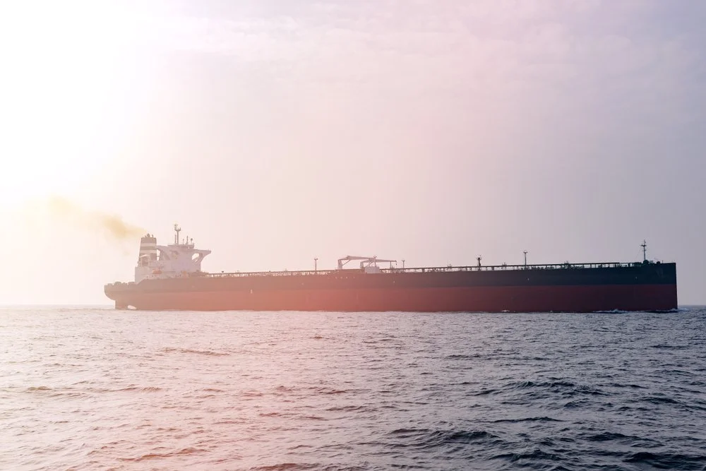 Large cargo ship sailing on the open sea during daylight with a slight haze in the sky.
