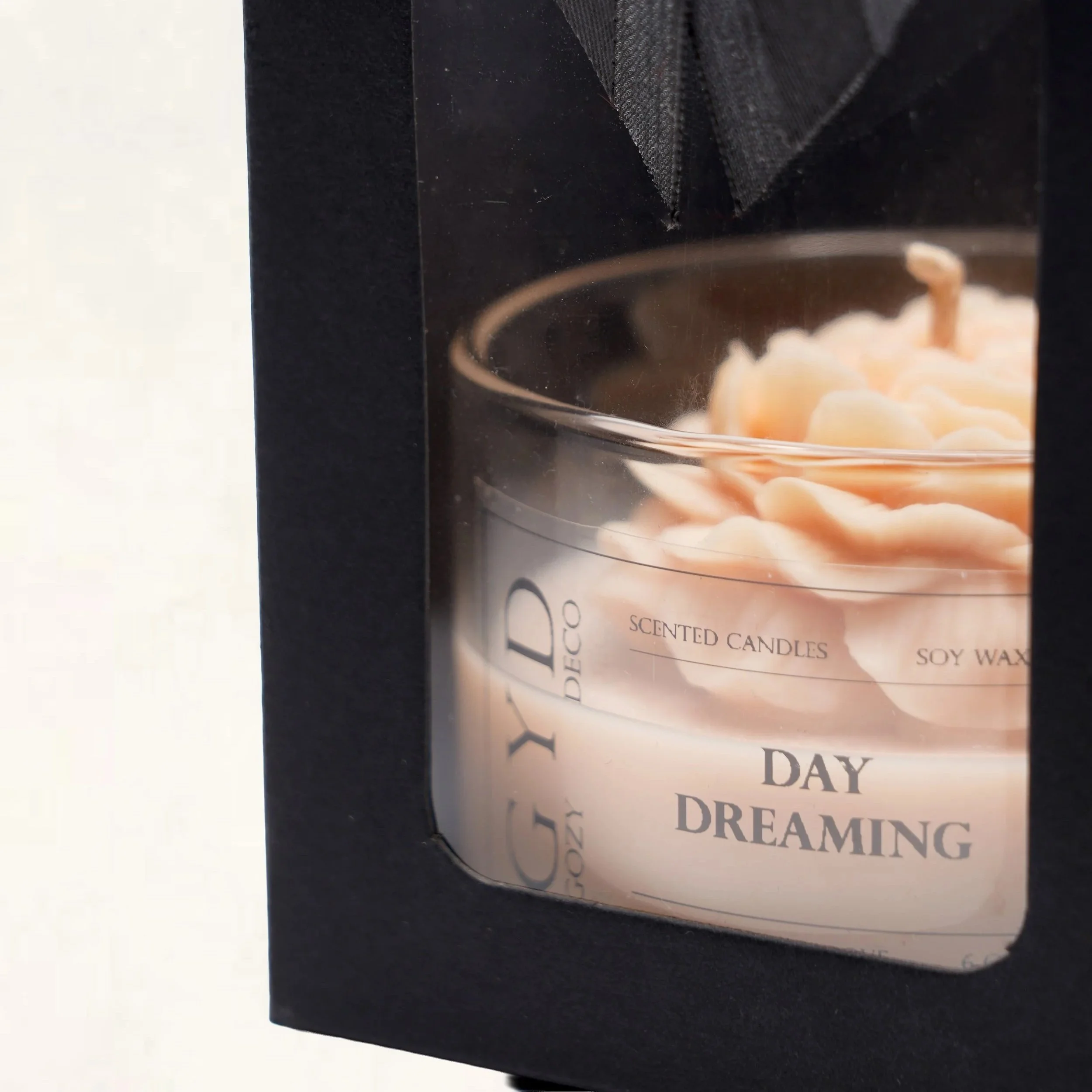 A scented candle labeled 'Day Dreaming' inside a black box with a clear window.