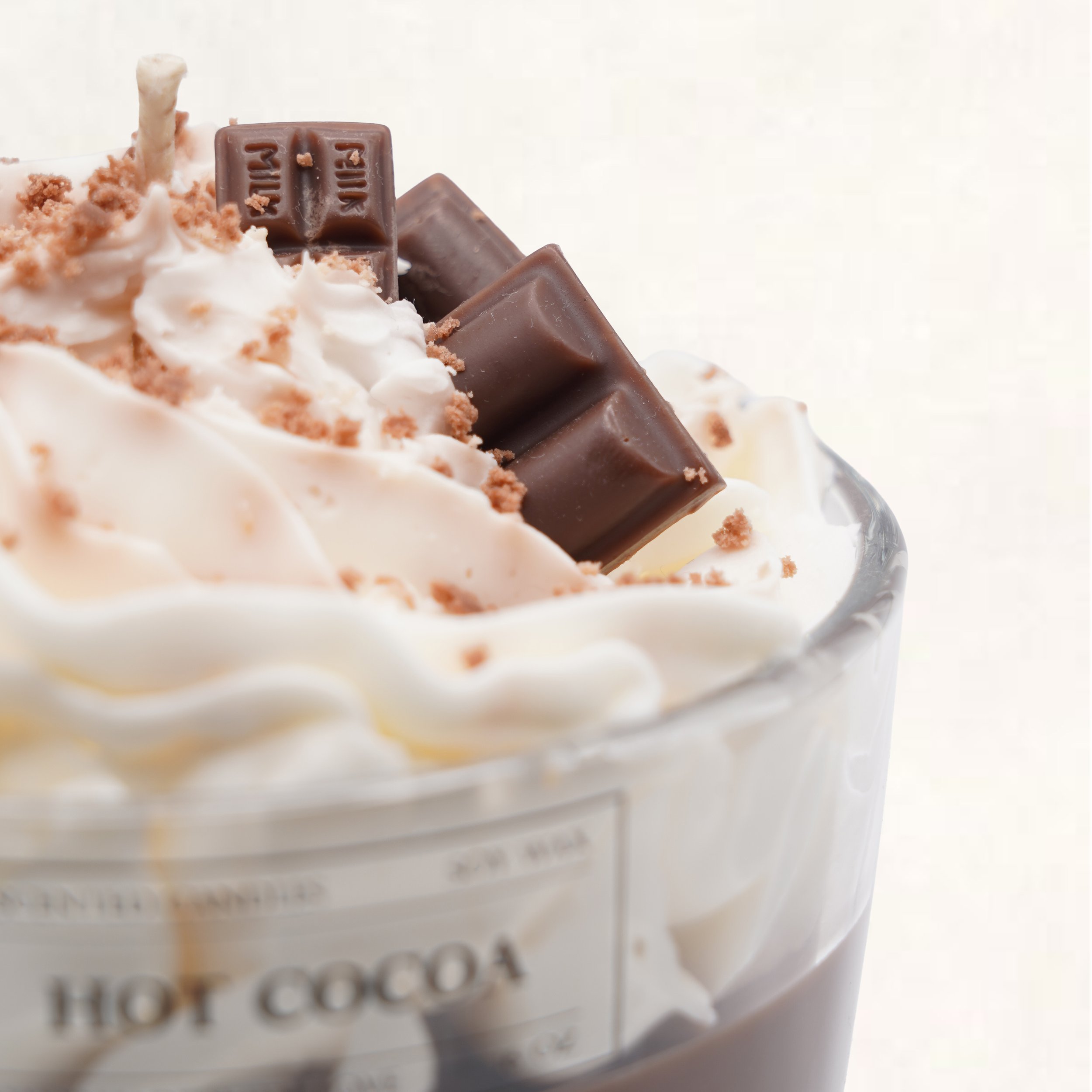 Close-up of a hot cocoa in a glass mug topped with whipped cream, chocolate chunks, and crumbs.