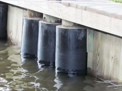 Close-up of three black rubber boat bumpers attached to a wooden dock, floating in the water to protect boats.