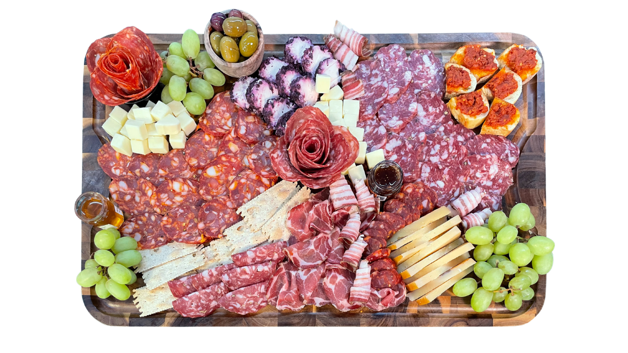 Charcuterie board with assorted meats, cheeses, grapes, olives, bread, and small toppings.