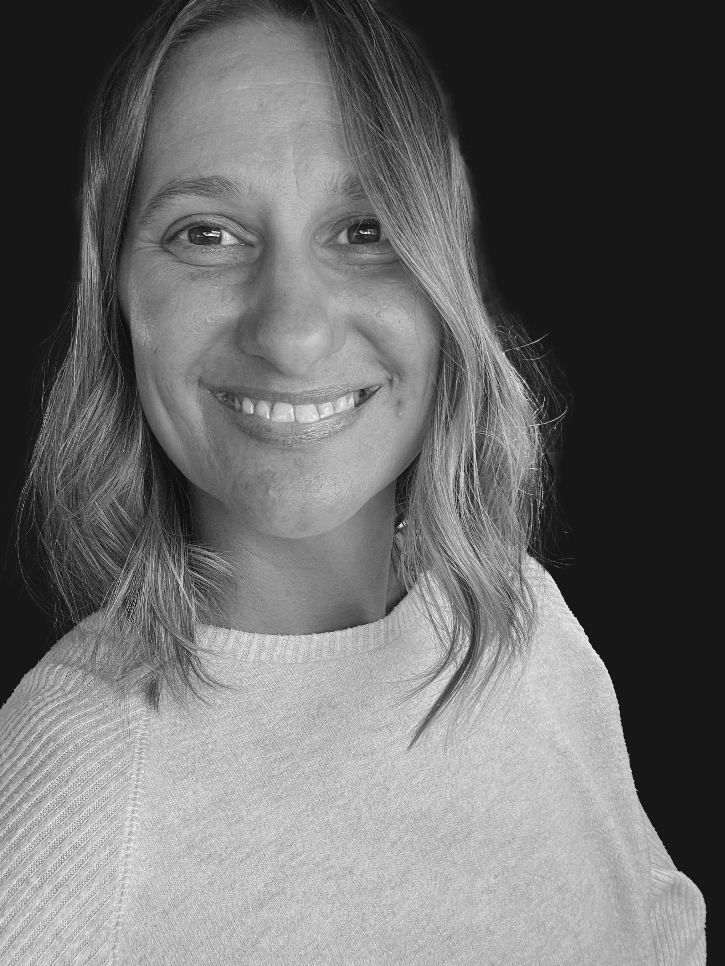 Black and white close-up portrait of a smiling woman with shoulder-length hair, wearing a light-colored top.