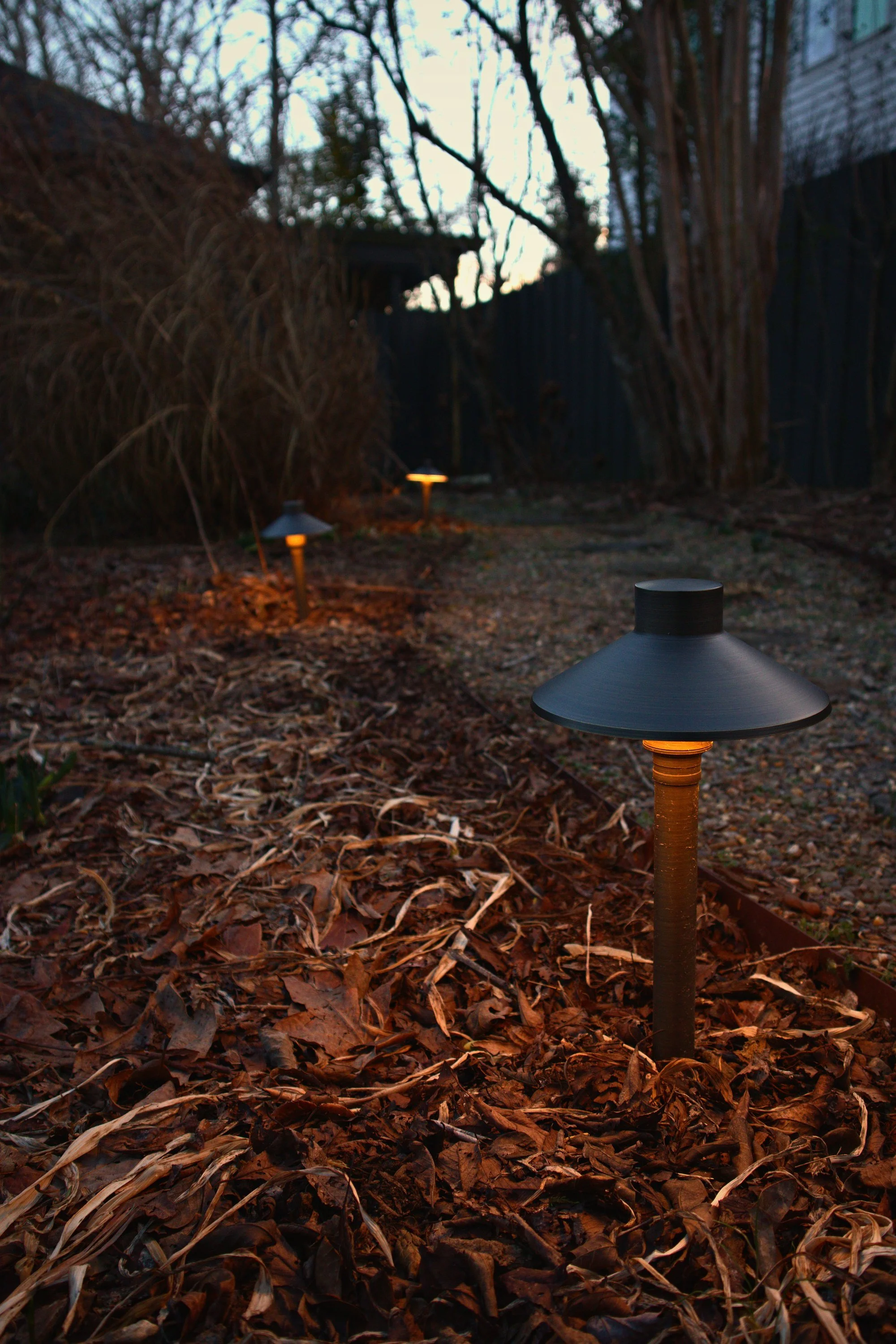 A twighlight shot of 3 low voltage landscape lighting fixtures.