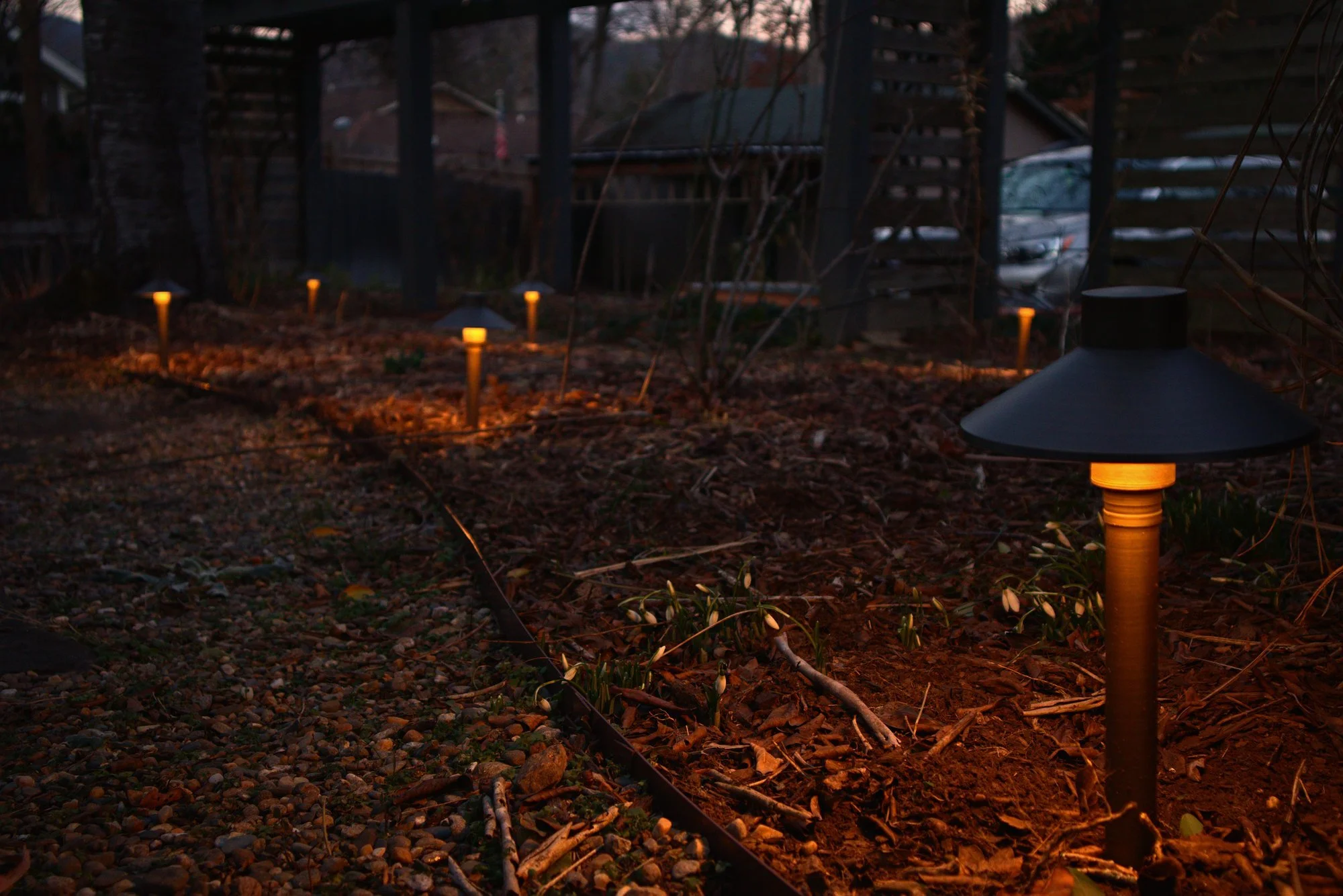 Evening photo of a series of outdoor low-voltage landscape lighting fixtures.
