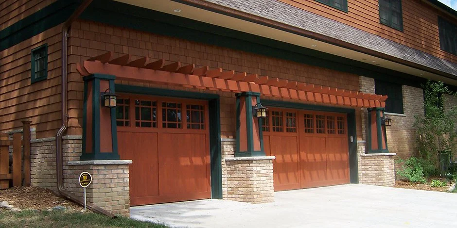 Wooden garage doors in Chaska with brick pillars and decorative pergola on a residential building's exterior.
