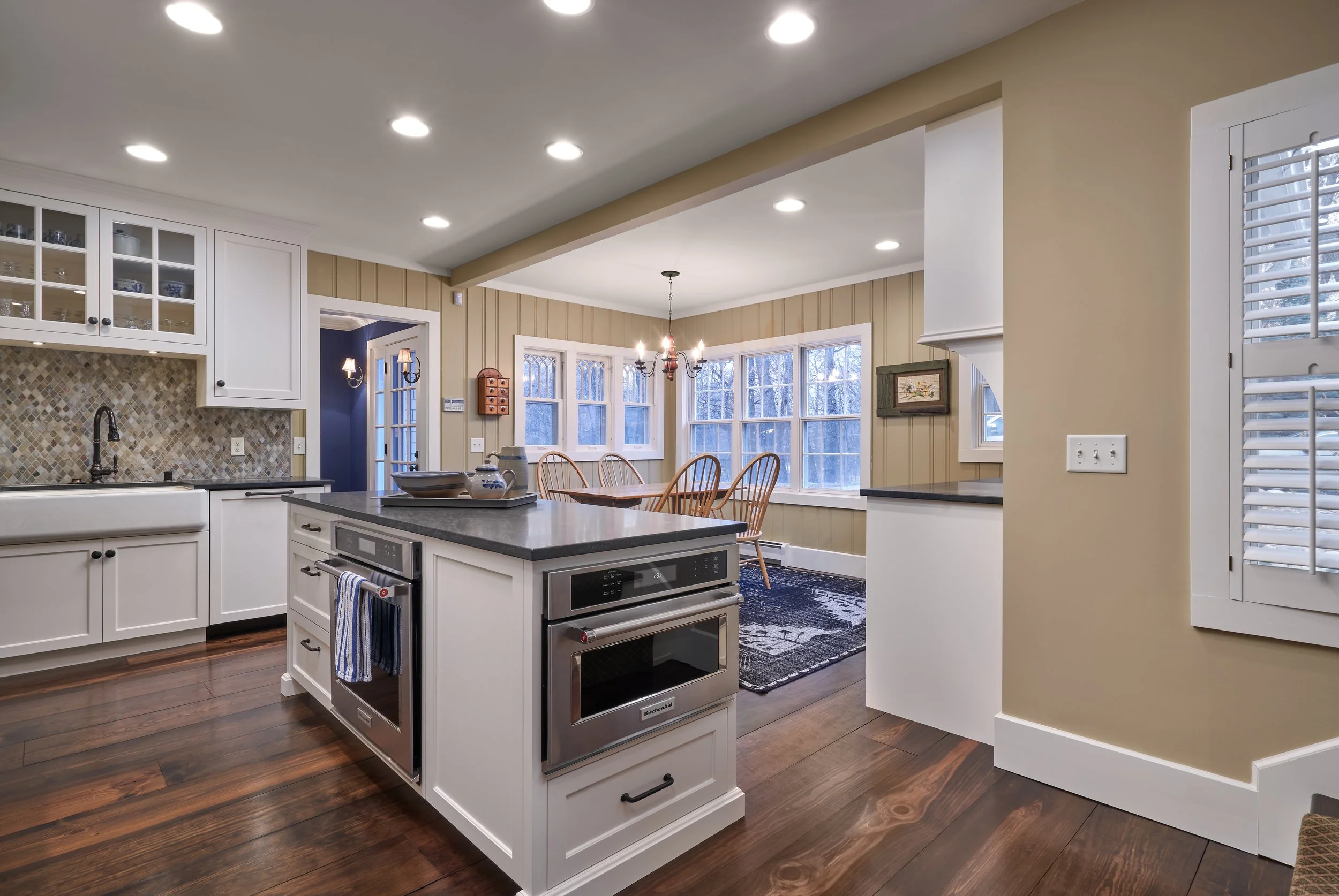 Modern kitchen  remodel in Excelsior with island, white cabinets, dark countertops, wood flooring, dining area, and large windows.