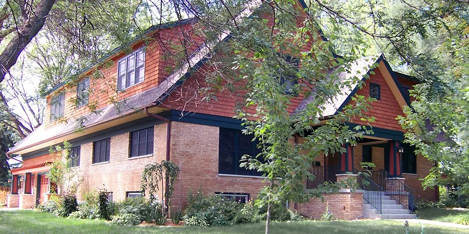 Two-story brick house remodel in Victoria with wood siding and gable roof surrounded by trees and greenery.