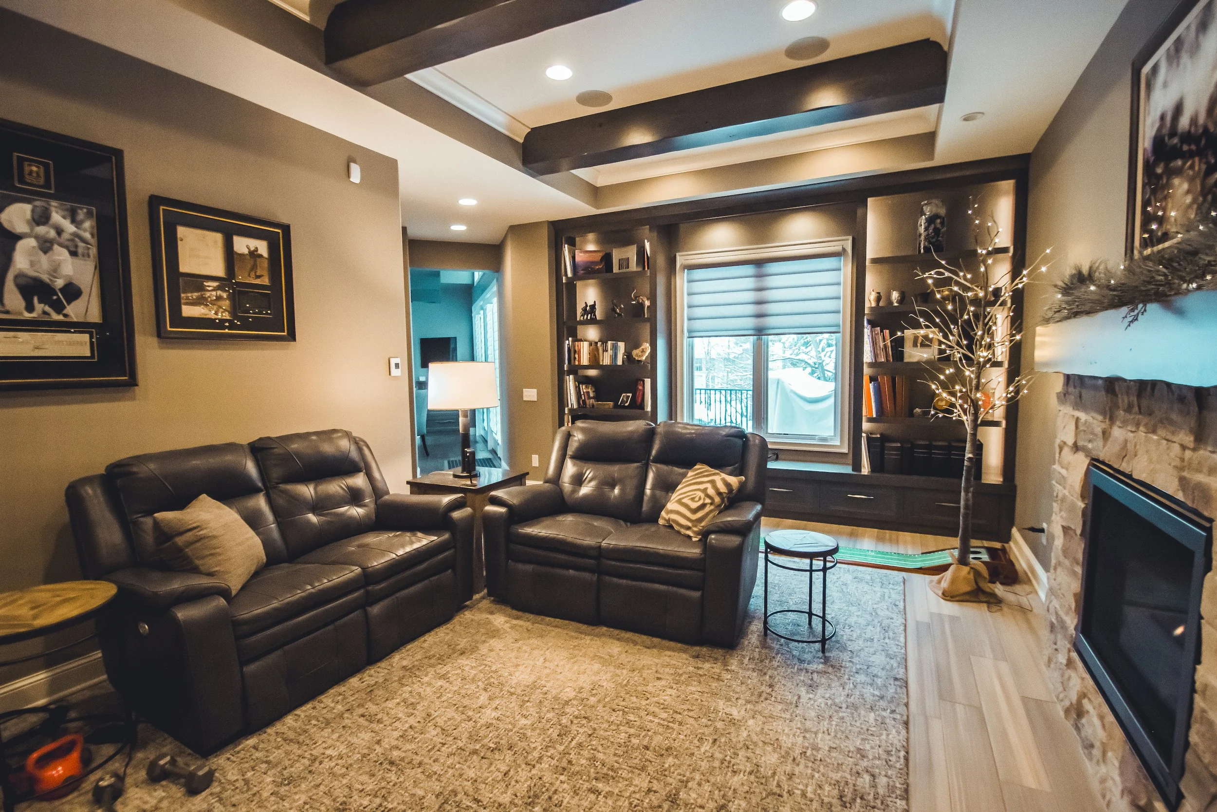 Cozy living room remodel in Victoria with dark leather sofas, bookshelves, and a fireplace.