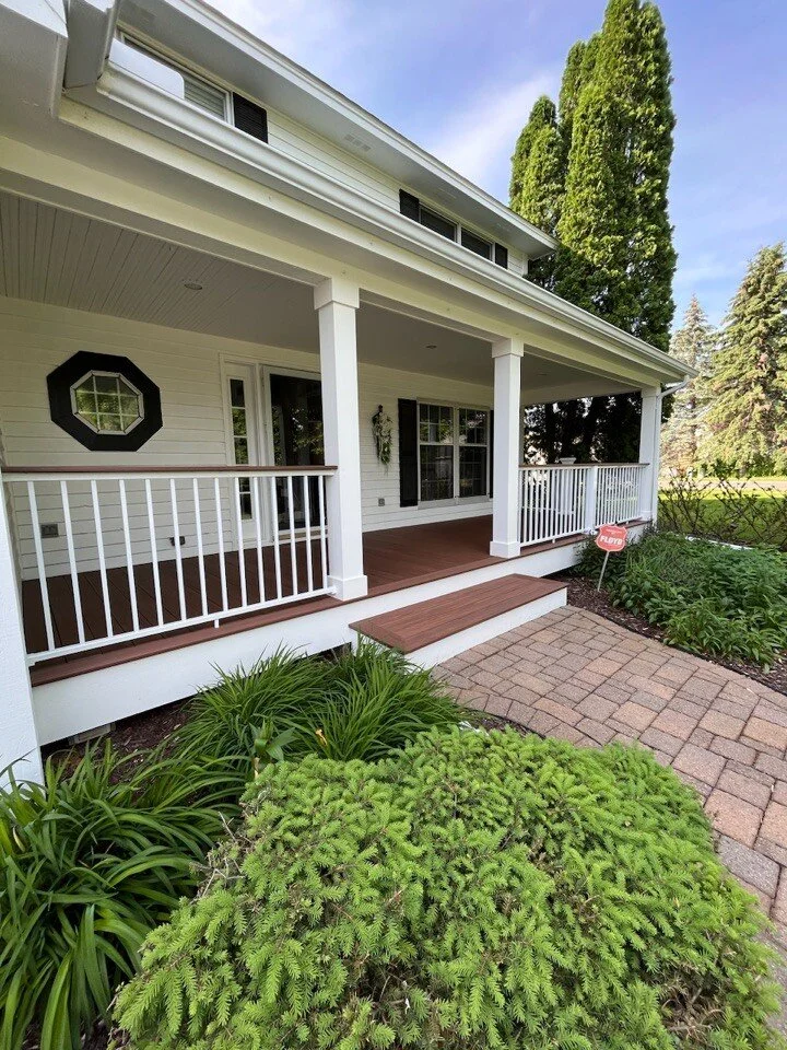 Front porch of a house  remodel in Excelsior with white railings, a brick path, and green landscaping. Large trees in the background.