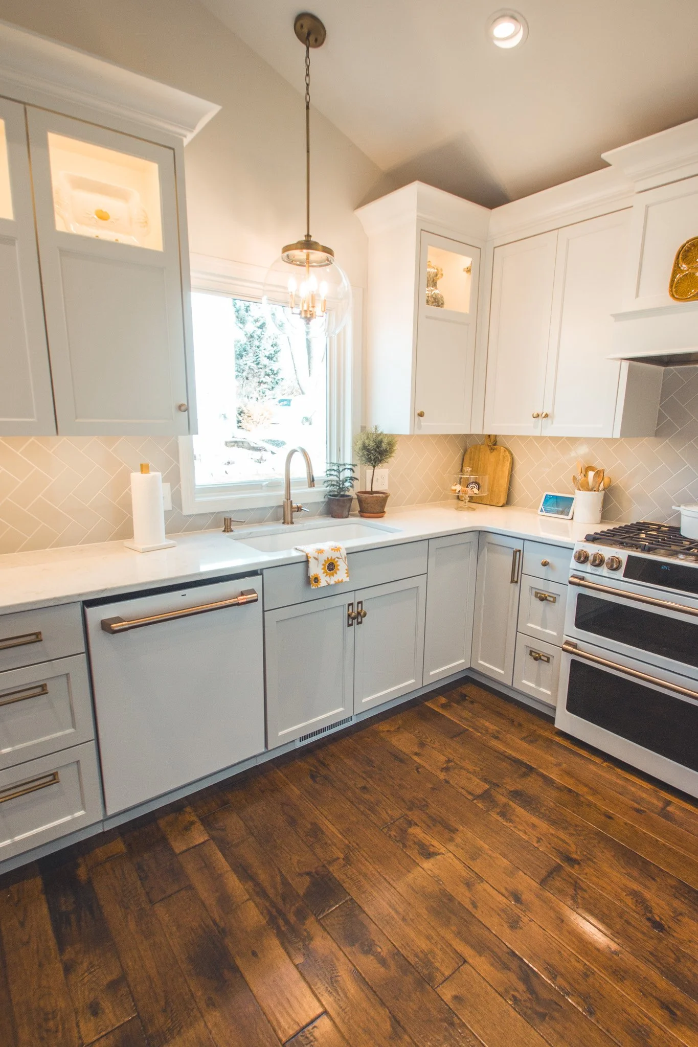 Modern kitchen remodel in Minnetonka with white cabinets, stainless steel appliances, pendant lighting, and wooden flooring.