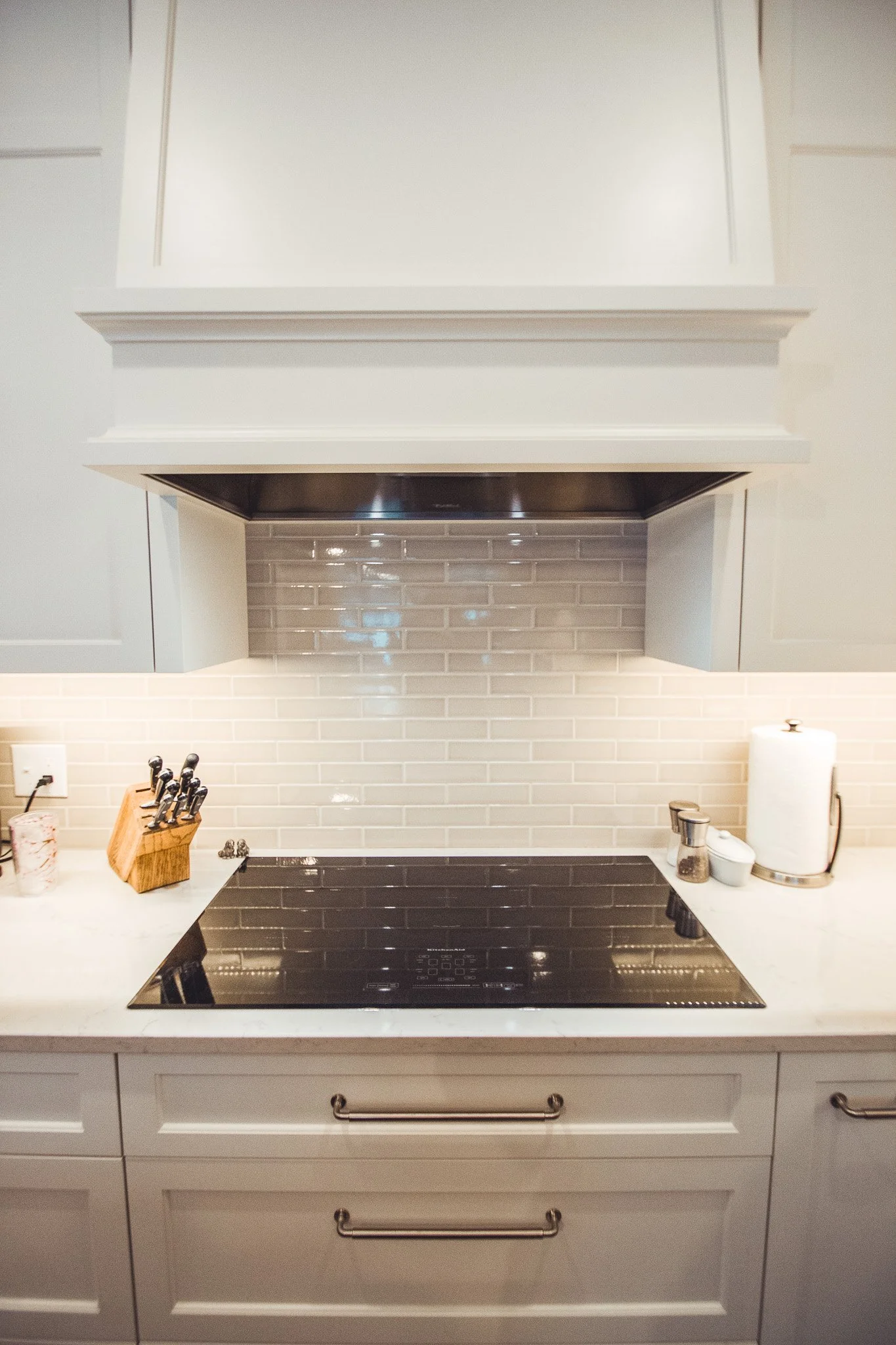 Modern kitchen remodel in Chanhassen with electric stove, white cabinets, tiled backsplash, knife block, pepper grinder, paper towel holder, and under-cabinet lighting.