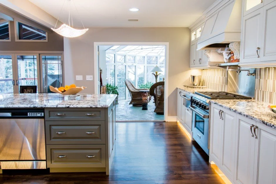 Modern kitchen remodel in Minnetonka with granite countertops, stainless steel appliances, and an island with fruit bowl, leading to a sunroom with wicker furniture.