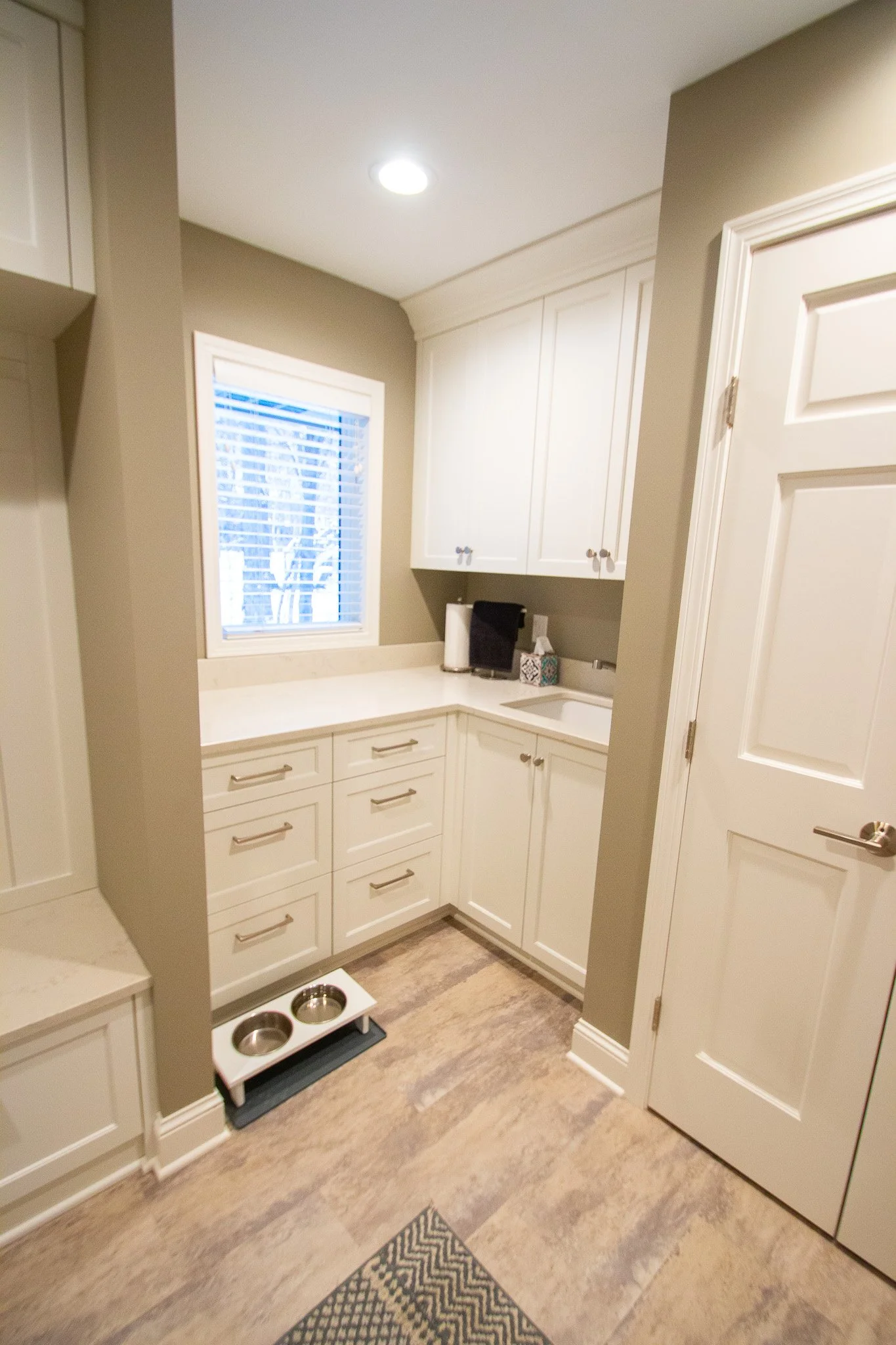 Laundry room remodel in Eden Prairie with white cabinets, sink, and dog bowls on tile floor.