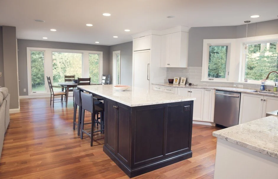 Open kitchen  remodel in Excelsior with white cabinets, dark island, wood floor, dining area with large windows.