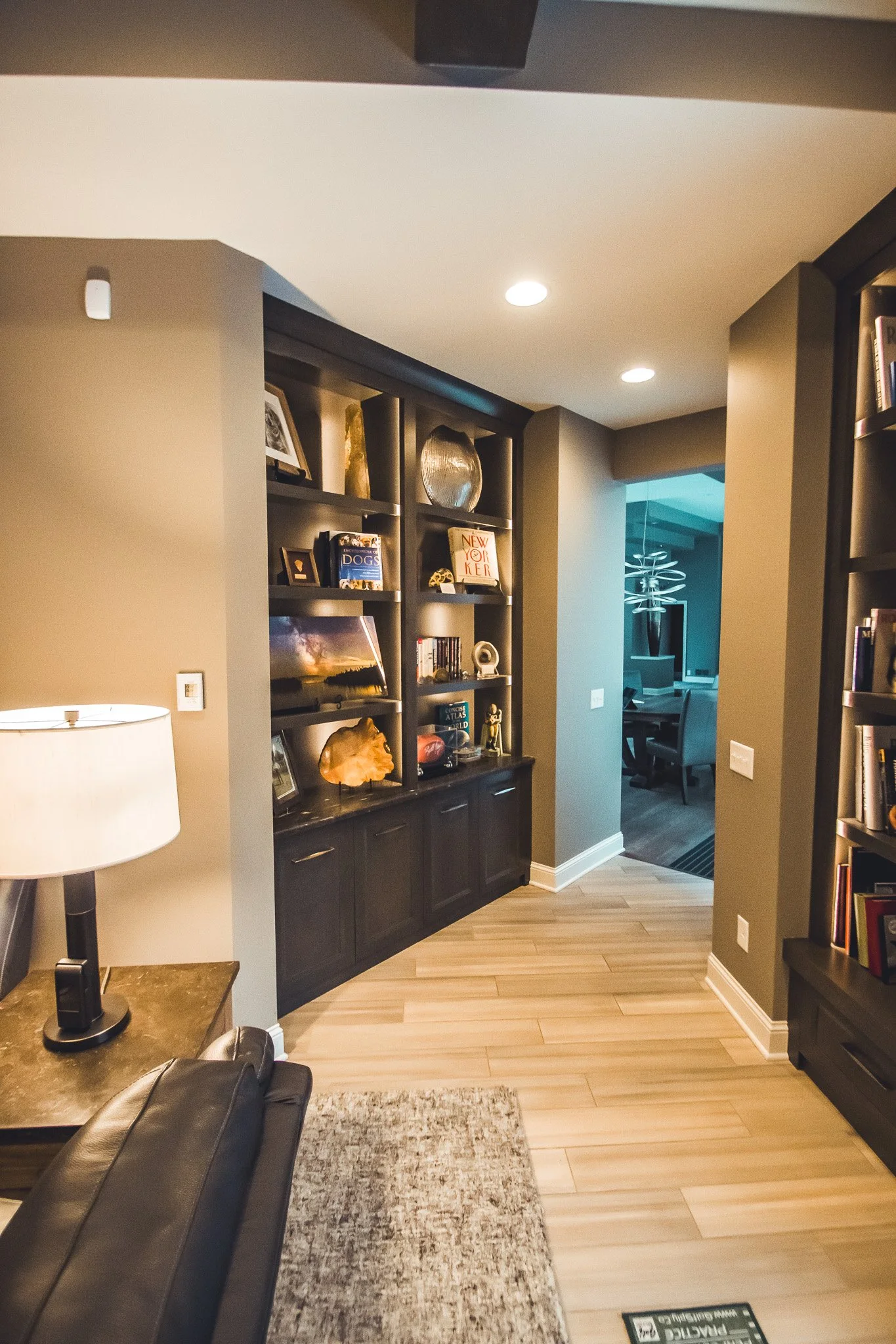 Cozy living space remodel in Minnetonka with built-in bookshelves filled with books, decorations, and a framed photo; a hallway leads to a modern dining area with unique lighting. 