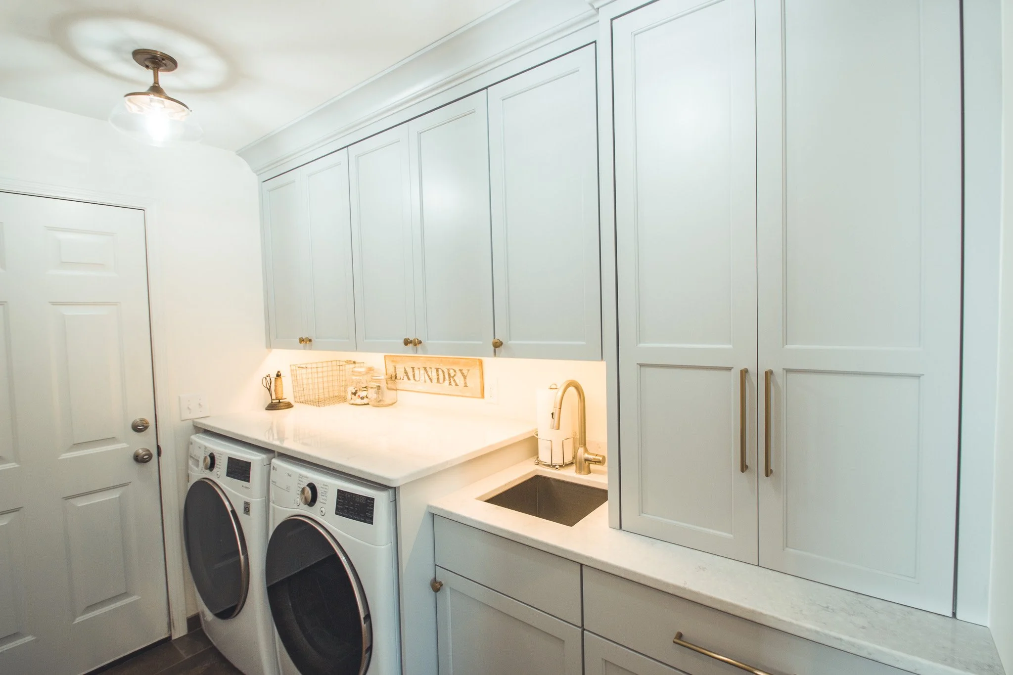 Modern laundry room remodel in Minnetonka with gray cabinets, washer and dryer, countertop, sink, and overhead light.
