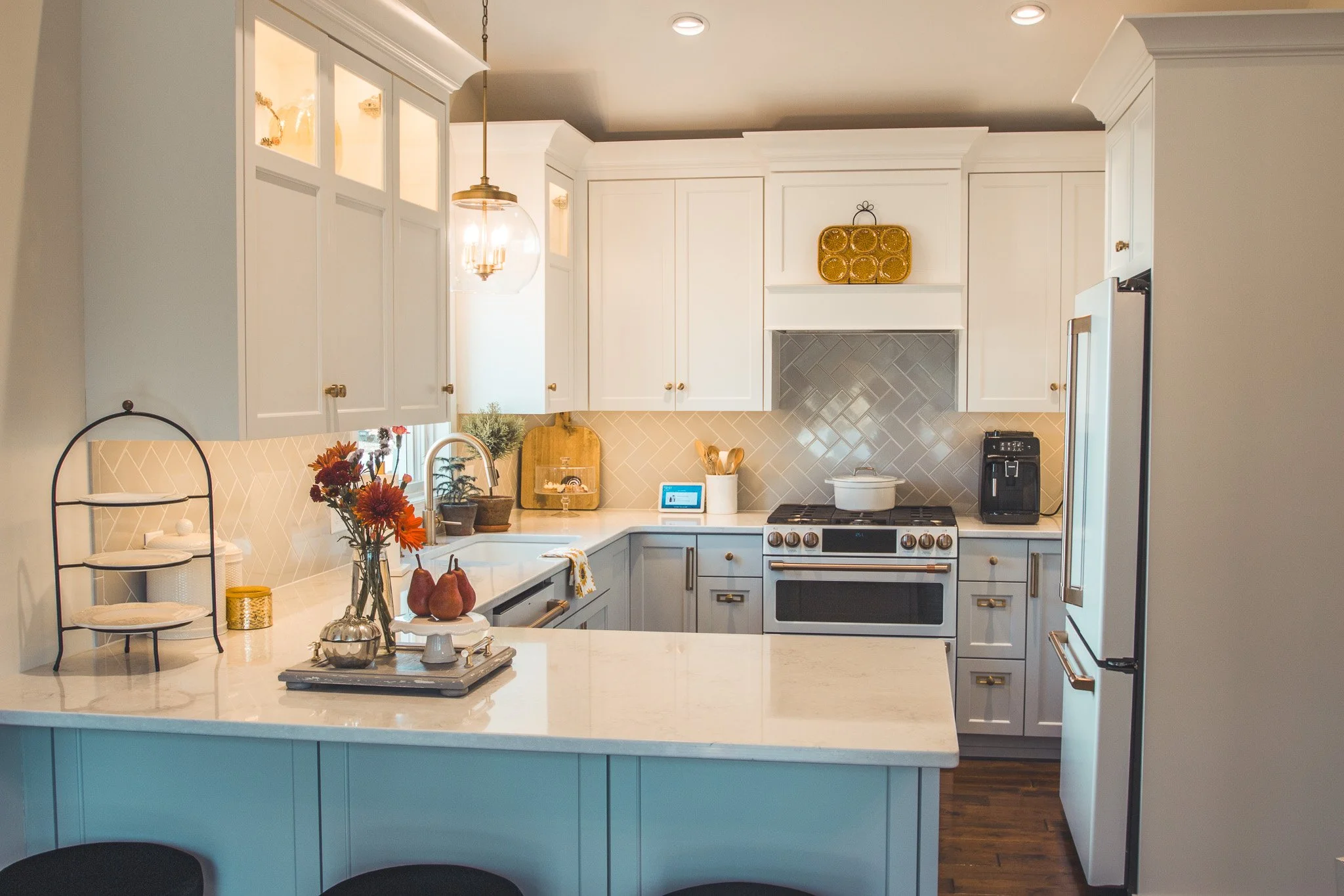 Modern kitchen Chanhassen with white cabinets, marble countertops, stainless steel appliances, backsplash tiles, decorative plants, and pendant lighting.