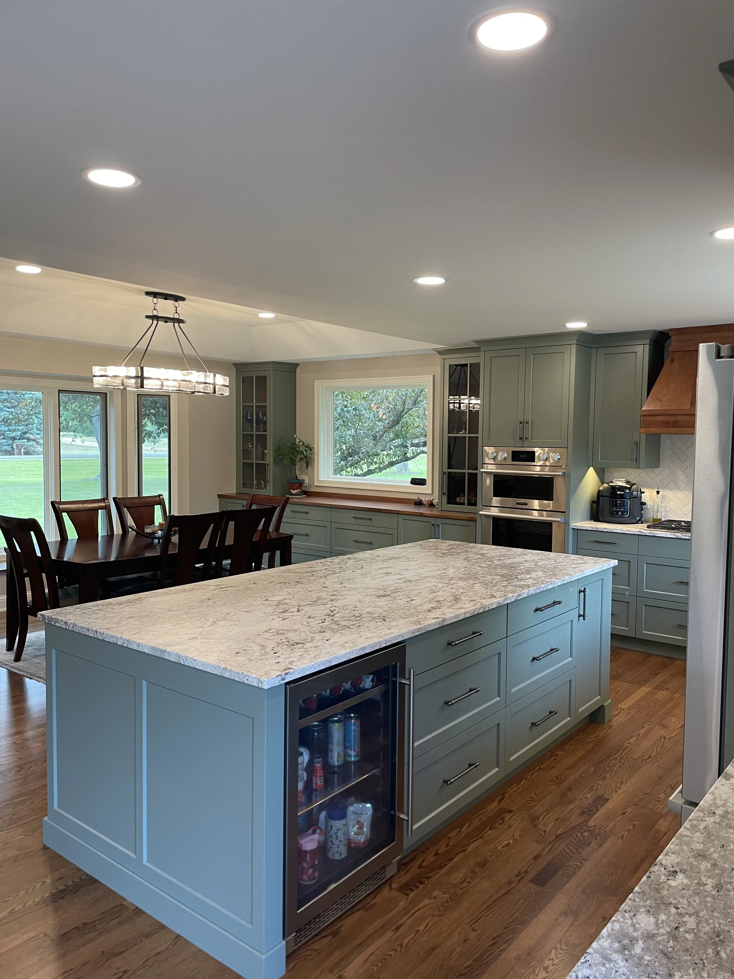 Modern kitchen in St. Louis Park with a large island featuring blue cabinetry and a built-in beverage cooler. Light fixtures are recessed into the ceiling. 