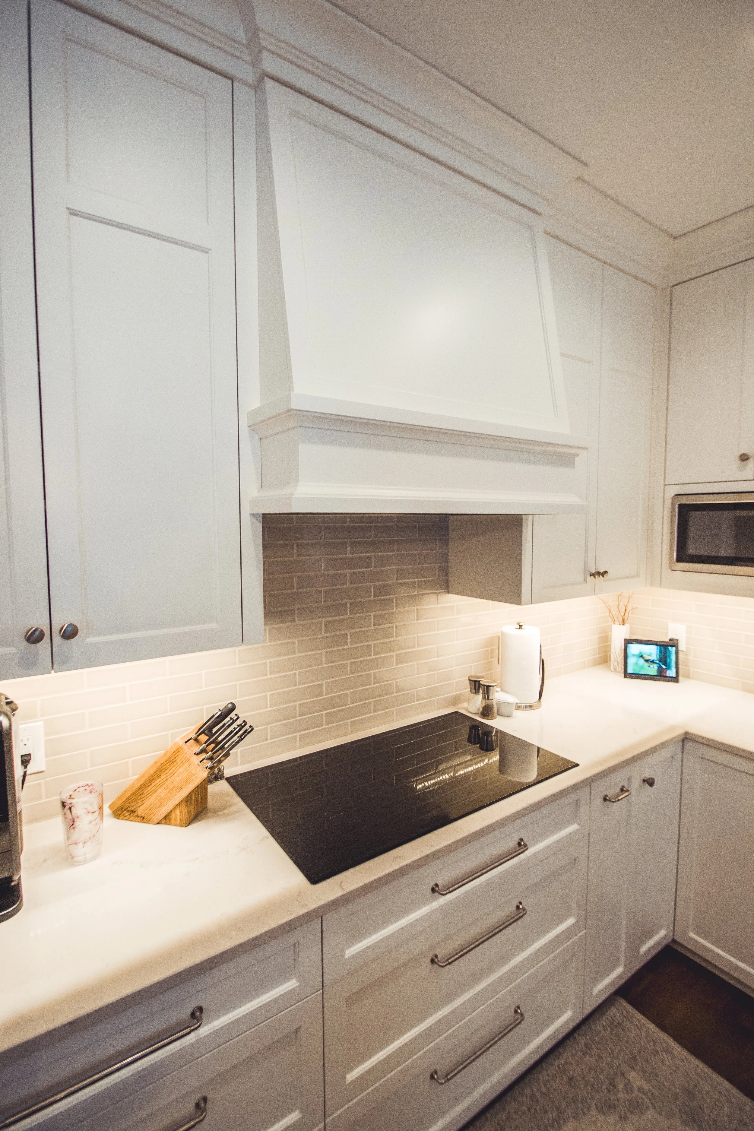 Modern kitchen in Minneapolis with white cabinets, a flat electric stovetop, a knife block, light-colored brick backsplash, and under-cabinet lighting.