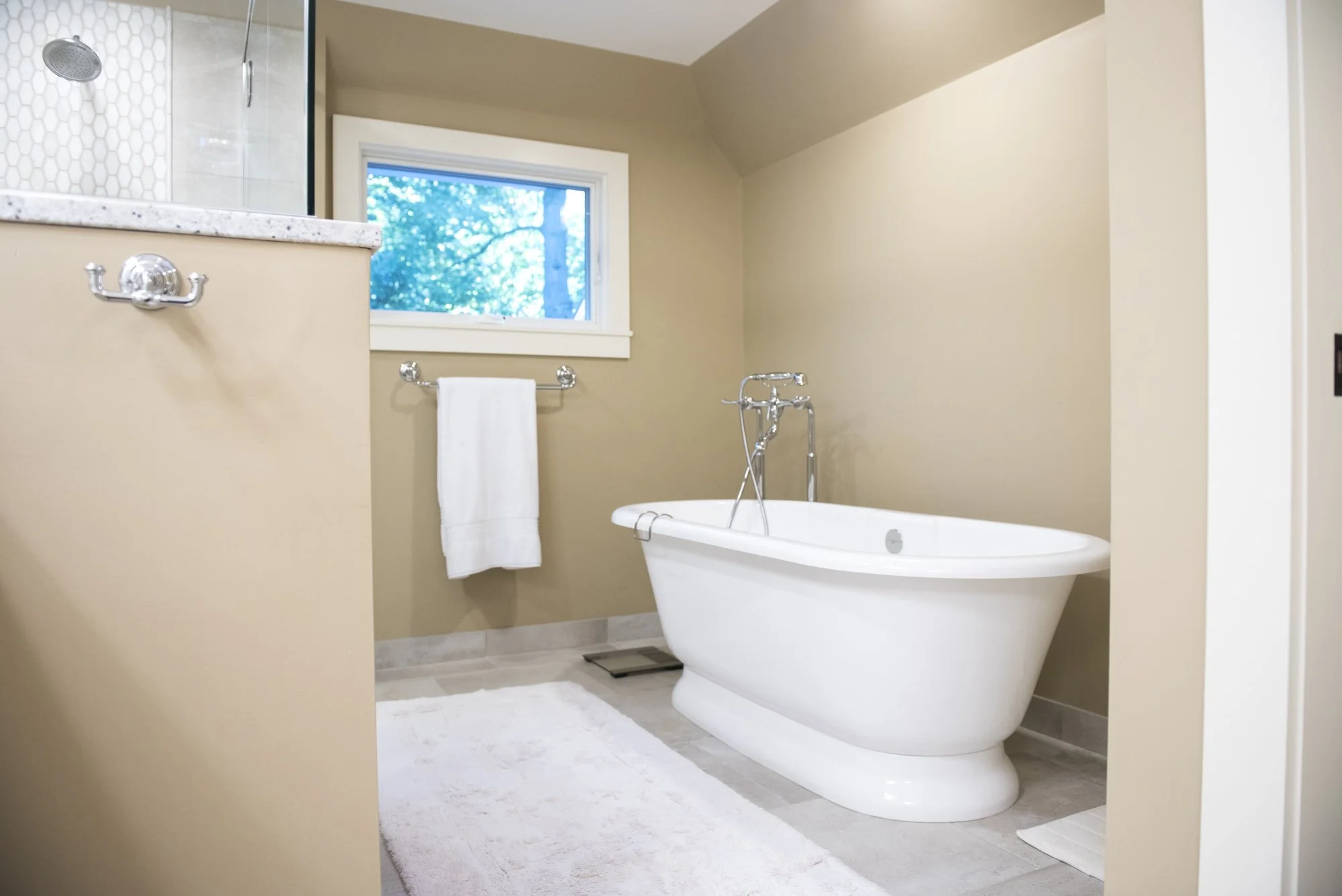 Modern bathroom  in Chanhassen with freestanding bathtub, shower with glass enclosure, window view, towel rack with white towel, and beige walls.