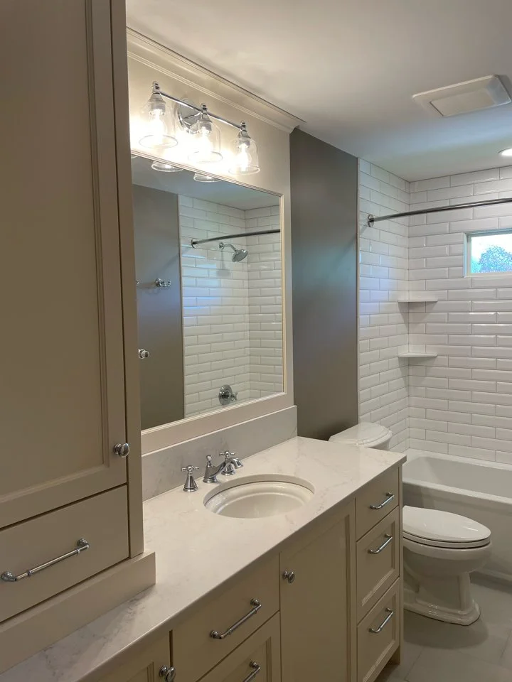 Modern bathroom remodel in Chanhassen with a white countertop, built-in sink, light fixtures above a large mirror, and a bathtub-shower combination. The walls are tiled with white subway tiles.