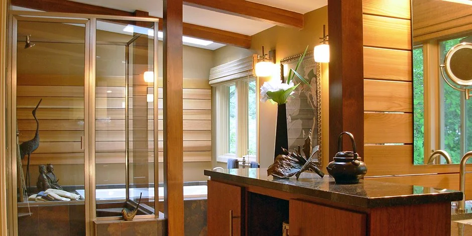 Modern bathroom remodel in Chanhassen with wooden paneling, a glass shower enclosure, and a large mirror. The space features a black countertop with decorative items and warm lighting.