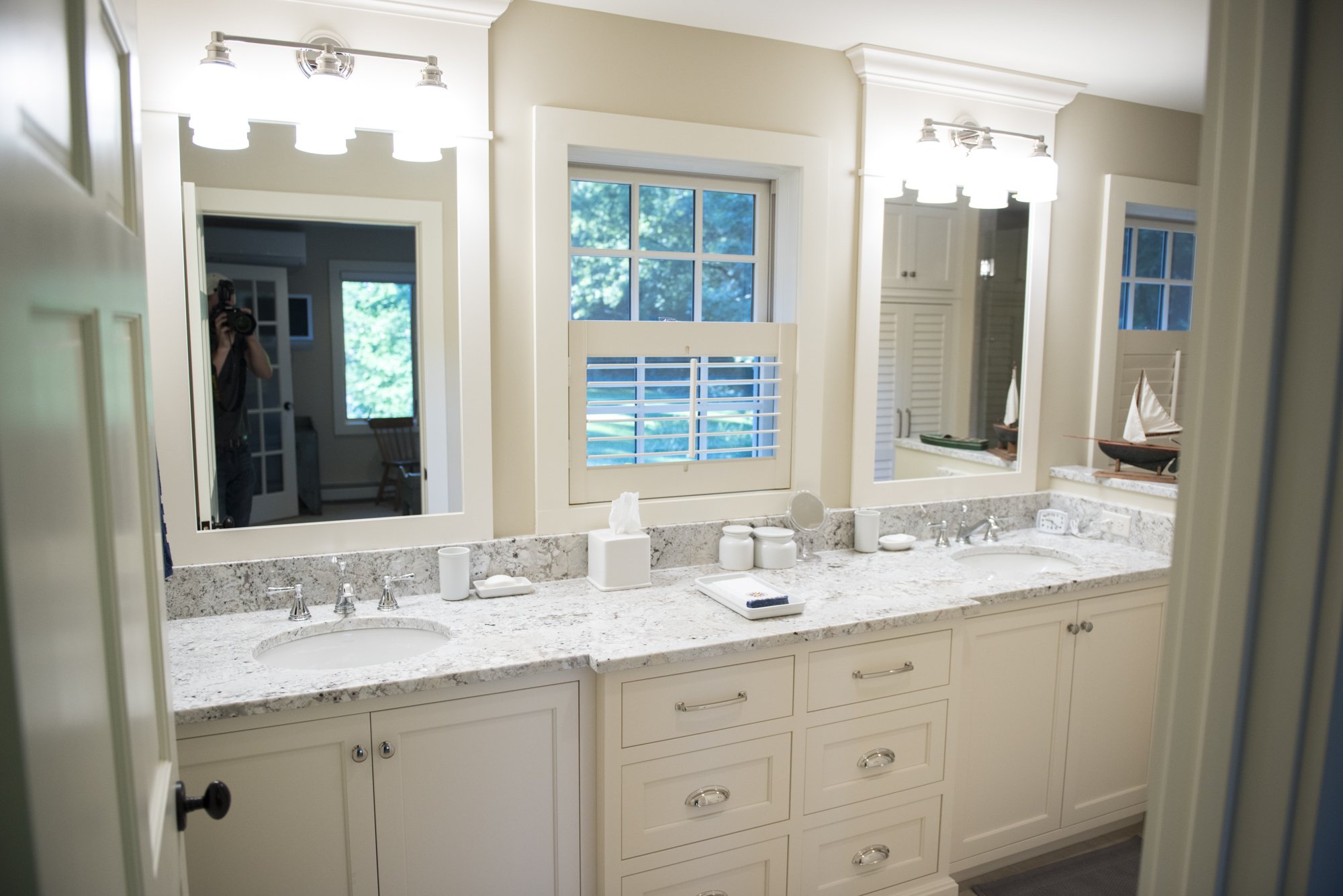 Modern bathroom  in Chanhassen with double sink vanity, granite countertop, large mirrors, and windows with shutters. Includes white cabinetry, decorative sailboat, and soft lighting.