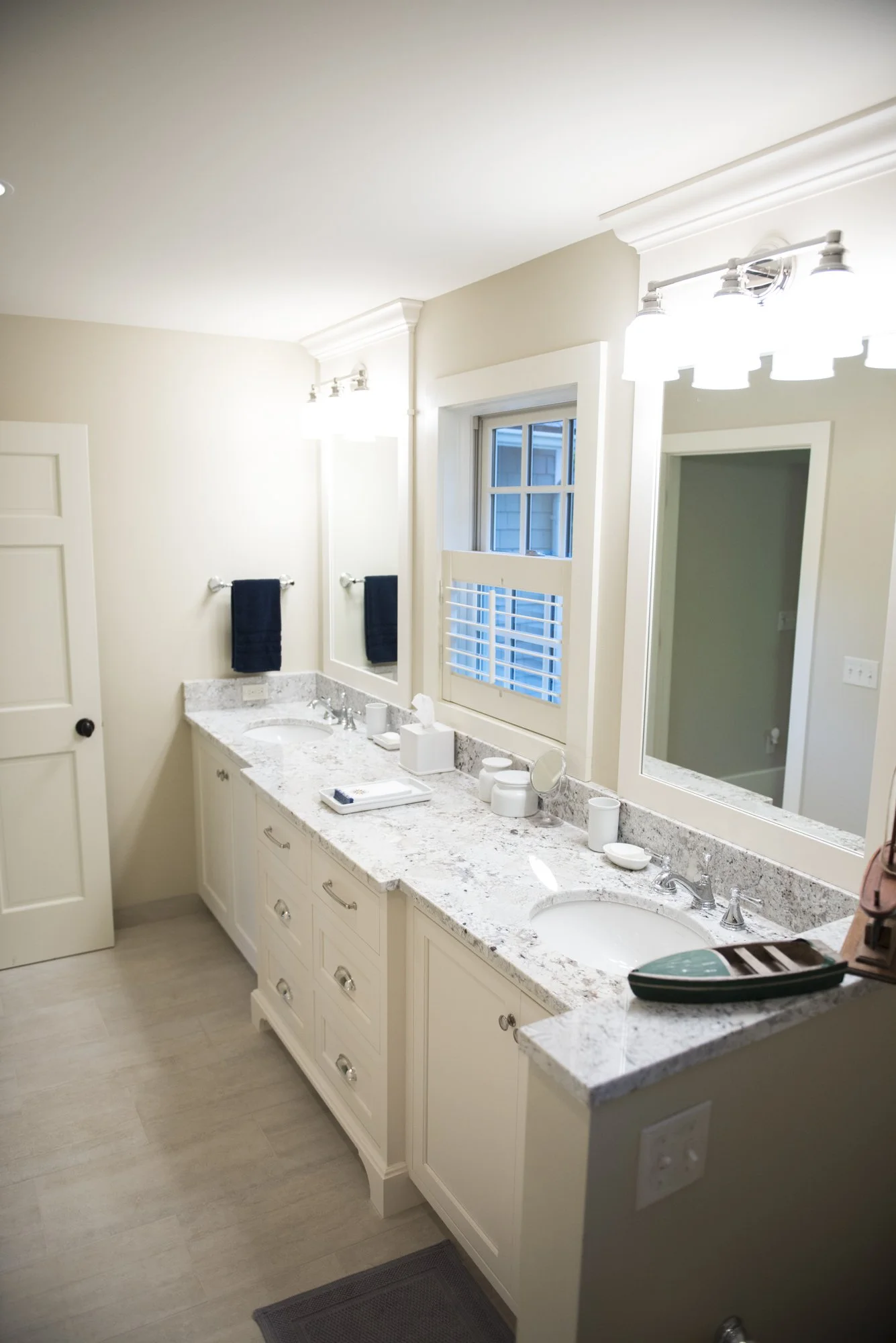Modern bathroom  in Chanhassen with double vanity and granite countertops, featuring two sinks, large mirrors, light fixtures, and a window with blinds.