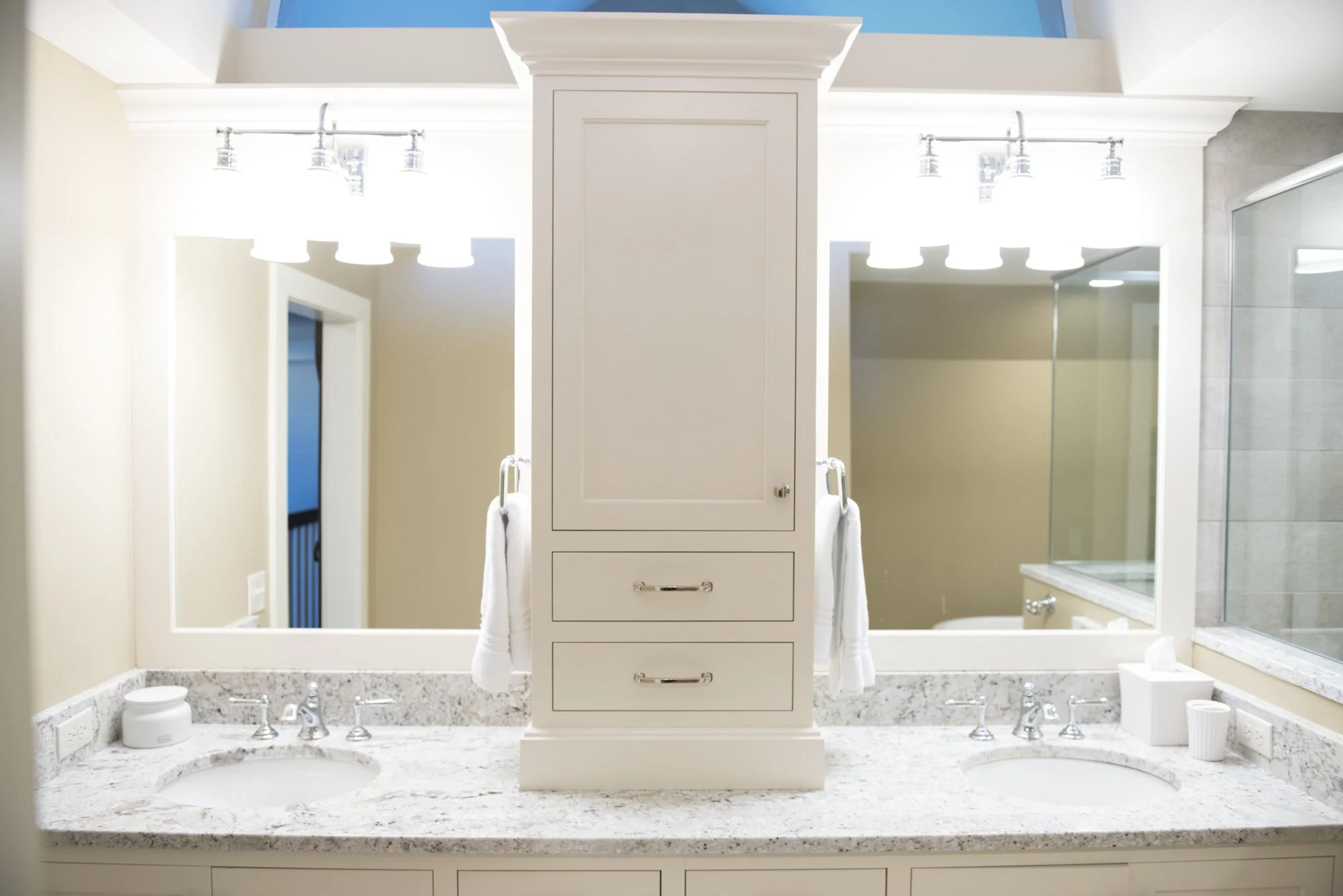 Modern bathroom  in Chanhassen vanity with two sinks and a central cabinet, surrounded by mirrors and overhead lighting, featuring marble countertops and chrome faucets.