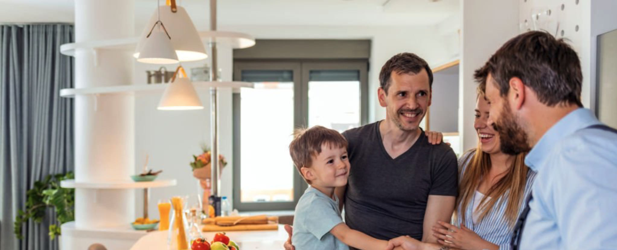 A family with a young child greeting a visitor in a modern kitchen during a at home consultation.